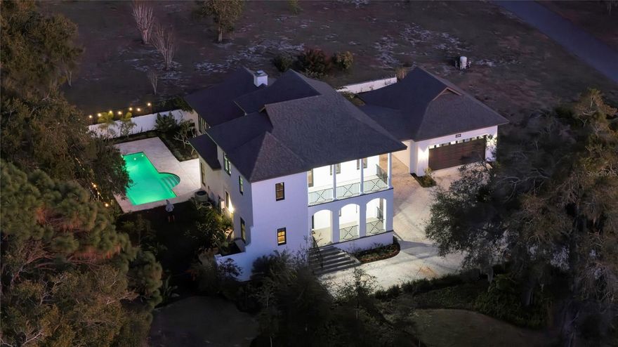 Perched atop a gentle rise and introduced through a private gated entry, this like-new 2023 custom estate is a refined expression of British West Indies–inspired architecture, crafted with enduring concrete block and stucco construction. Set on an expansive 1.21-acre homesite with no HOA, the property offers rare freedom, privacy and versatility, an exceptional opportunity to curate a lifestyle uniquely your own. Just moments from the heart of historic Mount Dora, residents enjoy effortless access to an enchanting collection of independent bookstores, cafés, acclaimed dining, art studios, waterfront festivals and year-round cultural events. Here, small-town charm meets elevated living. A glowing gas lantern sets a timeless tone as guests arrive on the welcoming front porch and go inside to a thoughtfully designed open floor plan, where architectural elegance and modern comfort coexist seamlessly. The chef’s kitchen is striking and functional, anchored by a substantial center island and featuring gas cooking, a butler’s pantry, serving center and café, ideal for intimate gatherings or grand entertaining. The kitchen flows effortlessly into the living room, where an Isokern masonry fireplace creates a warm focal point. Walls of Andersen windows and expansive sliding glass doors bathe the interior in natural light while framing tranquil views of the sparkling custom pool beyond, creating a seamless connection between indoor and outdoor living. The main level offers two generously sized bedrooms, ideal for multigenerational living or a private guest suite. The oversized primary retreat features a luxurious en-suite bath and walk-in closet, while secondary main-floor bedroom enjoys convenient access to the pool bath. Upstairs, a versatile loft with wet bar, full bath, and two additional large bedrooms provides a welcoming haven for family and guests. One bedroom opens to a private balcony, offering serene sunset views over the manicured grounds. A classic porte-cochere, accommodating two vehicles, gracefully connects the residence to an oversized two-car garage with a fully floored attic for abundant storage. Additional appointments include two gas water heaters, a whole-house standby generator, spray-foam attic insulation, and dual high-efficiency HVAC systems, ensuring comfort and energy efficiency throughout the home. Outdoors, a thoughtfully placed herb garden sits near the kitchen, while a flourishing fruit tree orchard enhances the backyard’s natural beauty and charm. Known as the crown jewel of Lake County and the Harris Chain of Lakes, Mount Dora offers an unparalleled lifestyle of waterfront recreation, cultural richness and effortless connectivity. With convenient access to the 453 Connector and Wekiva Parkway, all Central Florida lies within easy reach.