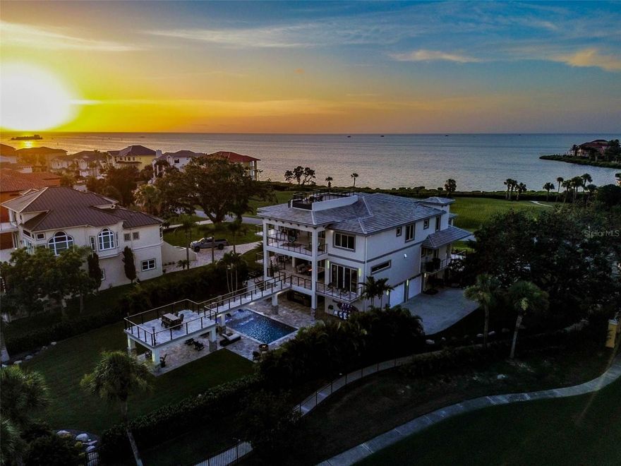 Welcome to coastal living at its finest. Tucked in a private, double-gated community on the stunning shores of the Gulf of Mexico, this one-of-a-kind, 3-story modern concrete estate offers unmatched strength, elegance, and serenity. Thoughtfully constructed with enduring concrete block slab, walls, floor, this home is as solid as it is spectacularly designed to withstand time and elements while delivering a lifestyle of elevated comfort and peace of mind. From the moment you arrive, the grand circular driveway, framed by a tranquil koi pond and towering architectural presence, sets a tone of sophistication and permanence. This home was built to impress and built to last. Inside, a private elevator effortlessly connects all three floors, blending everyday ease with luxury. The main living area is anchored by a stunning great room, where a dramatic Versace marble accent wall features an inset fireplace, creating a bold yet refined focal point. This elegant space is complemented by uninterrupted water views framed through expansive 10-foot sliding glass doors that span the entire second level, seamlessly merging indoor and outdoor living. Also on the second level, the primary suite is a retreat, featuring an elegantly tiled accent wall with an inset fireplace, adding warmth and ambiance to the already serene space. Sweeping Gulf views pour in through 10-foot sliding glass doors, filling the room with natural light. The spa-inspired en-suite bath, wrapped in exotic stone, offers a luxurious double shower with multiple showerheads on both sides, dual rainfall fixtures, and an oversized jetted soaking tub an indulgent sanctuary designed for ultimate relaxation. Go outside onto a one-of-a-kind walkway bridge that gracefully spans over the saltwater pool and spa, connecting the second level to the beautifully landscaped backyard. This resort-style design feature enhances the indoor-outdoor flow while offering breathtaking views of cascading water and lush tropical surroundings. Upstairs on the third floor, you'll find five generously sized guest bedrooms, three full baths, a waterfront fitness room, and a spacious bar and game room arranged for entertaining and unwinding. At day’s end, retreat to the private rooftop lookout to take in the panoramic Gulf views and unforgettable sunsets. For car collectors and enthusiasts, the garage offers space for up to eight vehicles and includes a rare professional-grade oil change and mechanic’s pit. A whole-home Generac generator ensures full power during any storm or outage, adding another layer of comfort and confidence. From its concrete construction and hurricane-ready design to its refined finishes and Gulf-front setting, this exceptional estate offers the best of coastal living, delivering beauty and resilience in equal measures.