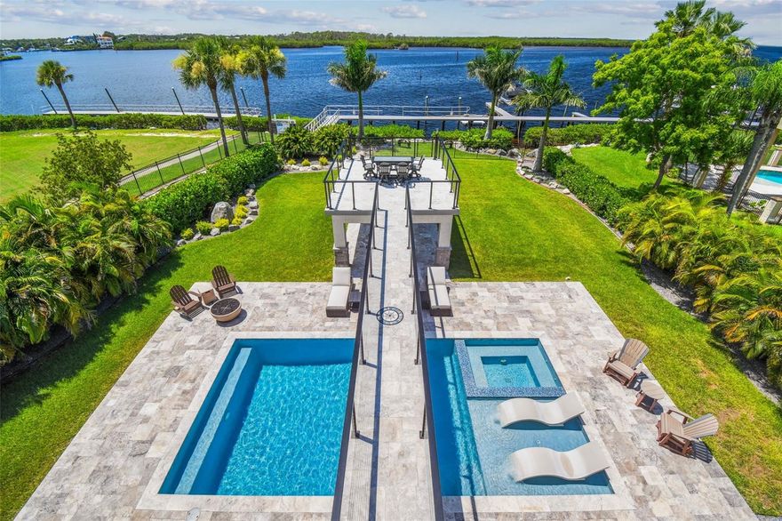 Welcome to coastal living at its finest. Tucked in a private, double-gated community on the stunning shores of the Gulf of Mexico, this one-of-a-kind, 3-story modern concrete estate offers unmatched strength, elegance, and serenity. Thoughtfully constructed with enduring concrete block slab, walls, floor, this home is as solid as it is spectacularly designed to withstand time and elements while delivering a lifestyle of elevated comfort and peace of mind. From the moment you arrive, the grand circular driveway, framed by a tranquil koi pond and towering architectural presence, sets a tone of sophistication and permanence. This home was built to impress and built to last. Inside, a private elevator effortlessly connects all three floors, blending everyday ease with luxury. The main living area is anchored by a stunning great room, where a dramatic Versace marble accent wall features an inset fireplace, creating a bold yet refined focal point. This elegant space is complemented by uninterrupted water views framed through expansive 10-foot sliding glass doors that span the entire second level, seamlessly merging indoor and outdoor living. Also on the second level, the primary suite is a retreat, featuring an elegantly tiled accent wall with an inset fireplace, adding warmth and ambiance to the already serene space. Sweeping Gulf views pour in through 10-foot sliding glass doors, filling the room with natural light. The spa-inspired en-suite bath, wrapped in exotic stone, offers a luxurious double shower with multiple showerheads on both sides, dual rainfall fixtures, and an oversized jetted soaking tub an indulgent sanctuary designed for ultimate relaxation. Go outside onto a one-of-a-kind walkway bridge that gracefully spans over the saltwater pool and spa, connecting the second level to the beautifully landscaped backyard. This resort-style design feature enhances the indoor-outdoor flow while offering breathtaking views of cascading water and lush tropical surroundings. Upstairs on the third floor, you'll find five generously sized guest bedrooms, three full baths, a waterfront fitness room, and a spacious bar and game room arranged for entertaining and unwinding. At day’s end, retreat to the private rooftop lookout to take in the panoramic Gulf views and unforgettable sunsets. For car collectors and enthusiasts, the garage offers space for up to eight vehicles and includes a rare professional-grade oil change and mechanic’s pit. A whole-home Generac generator ensures full power during any storm or outage, adding another layer of comfort and confidence. From its concrete construction and hurricane-ready design to its refined finishes and Gulf-front setting, this exceptional estate offers the best of coastal living, delivering beauty and resilience in equal measures.