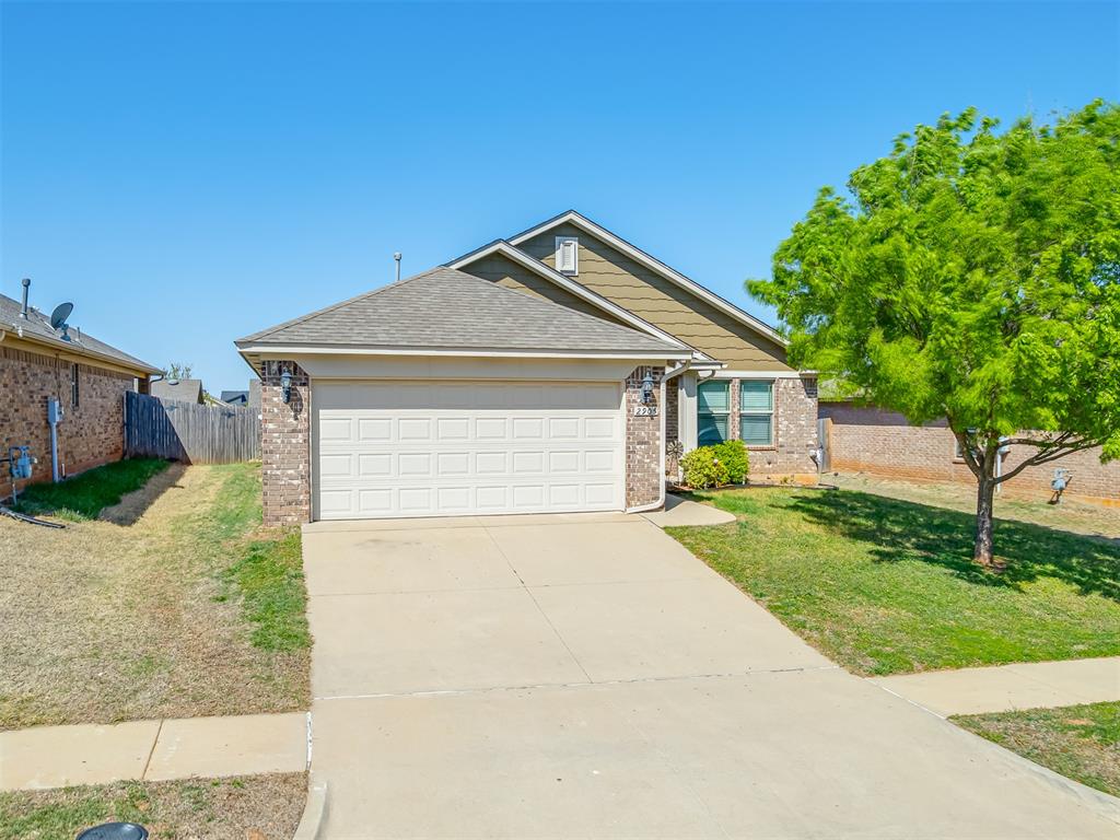 Brick and siding exterior with an attached garage, paved driveway, and mature landscaping