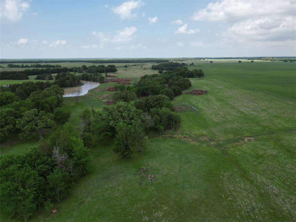 Expansive green acreage featuring a winding body of water, mature trees, and open fields under a broad sky