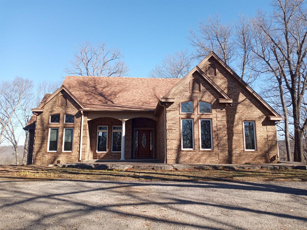 View of front of property featuring a porch, brick siding, and roof with shingles