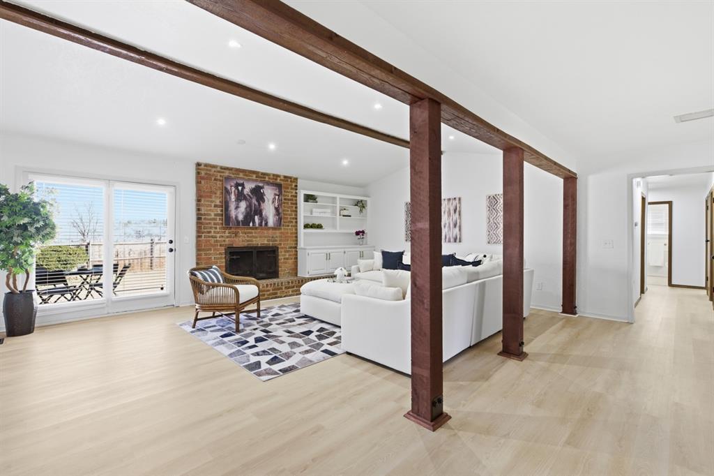 Living area with light wood-style flooring, a brick fireplace, beamed ceiling, built in features, and recessed lighting