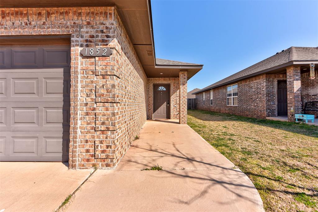 Property entrance featuring brick siding, a garage, a yard, and a shingled roof