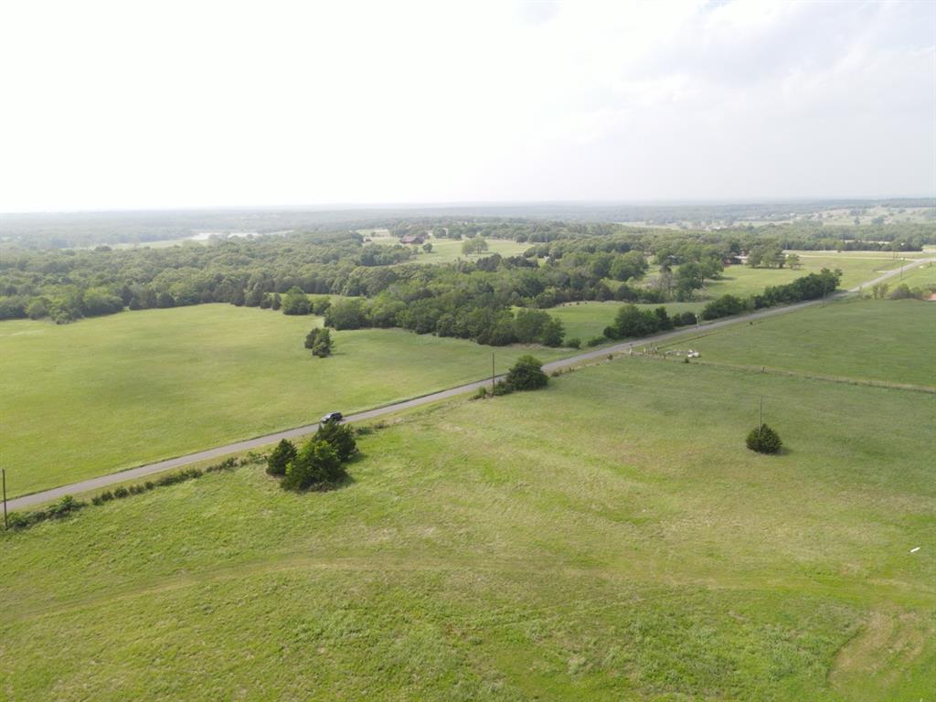 Expansive green pastureland featuring a natural pond, scattered mature trees, and varied terrain