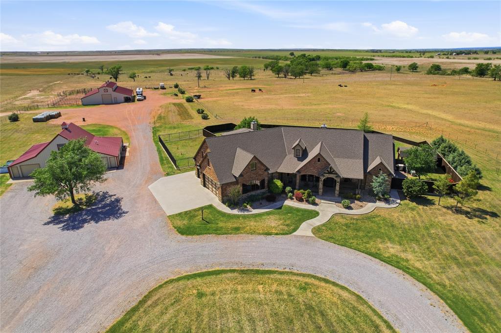 Expansive property featuring a stone and brick main residence with a concrete driveway and an additional outbuilding with red roofing