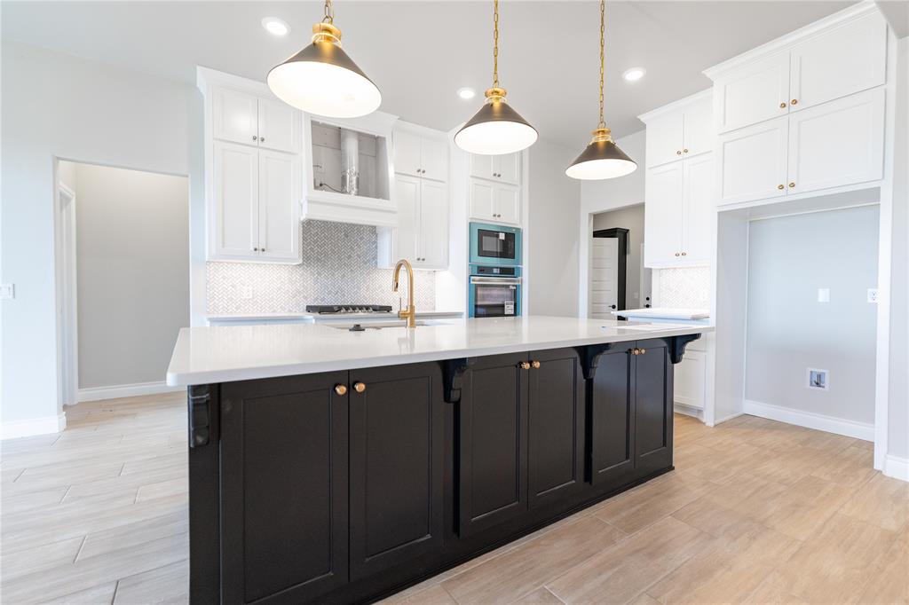 Kitchen featuring two tone cabinetry, decorative backsplash, wood tiled floors, an island with sink, and stainless steel appliances