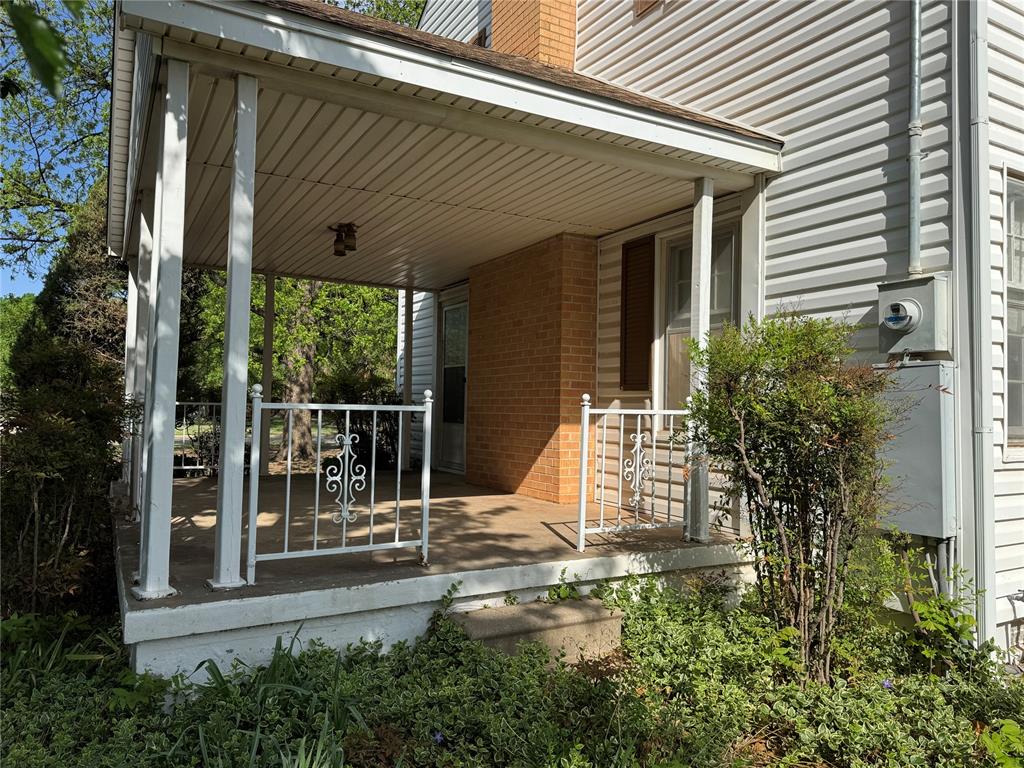 The property features a covered porch with white columns and decorative railings, set against a backdrop of established greenery and trees