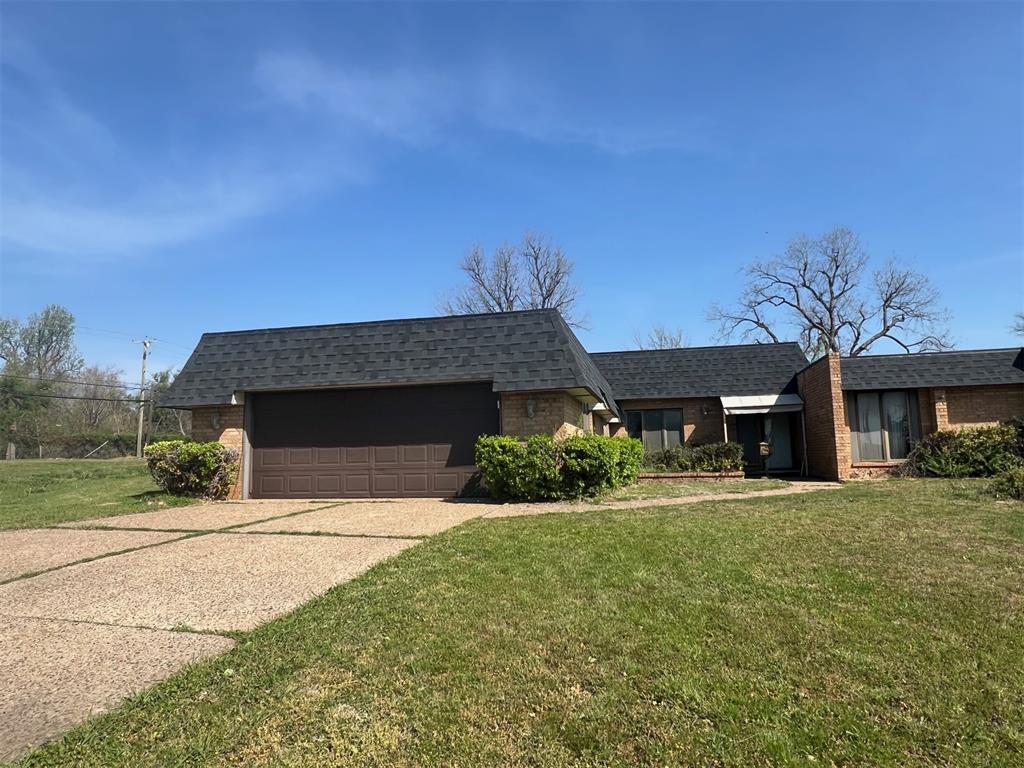 View of front of home with brick siding, concrete driveway, a front lawn, and a garage