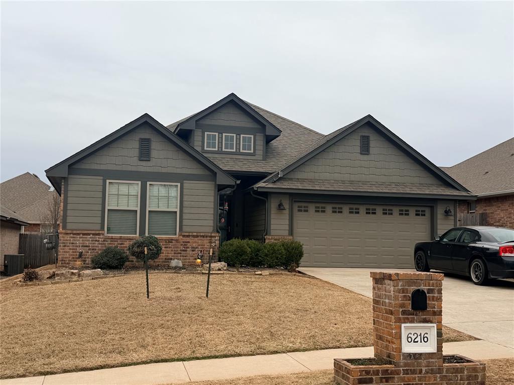 Craftsman-style home featuring roof with shingles, driveway, an attached garage, and brick siding