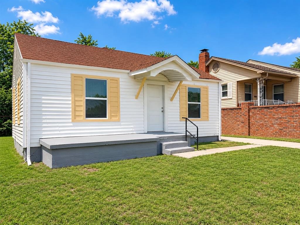 White siding exterior with a red shingle roof, yellow decorative shutters, a covered front entry, and a concrete porch with steps
