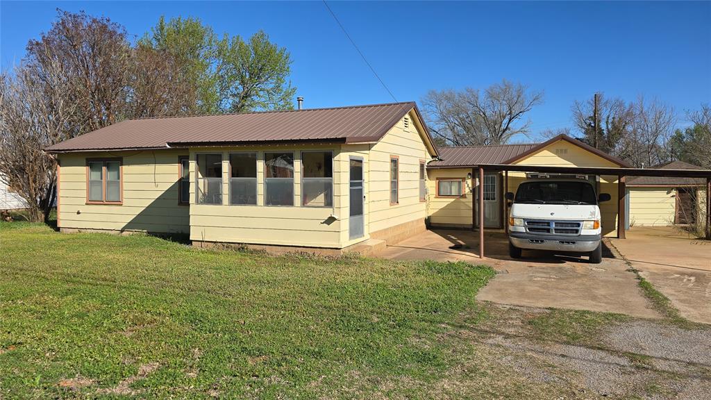 View of front facade featuring a front lawn, a metal roof, and driveway