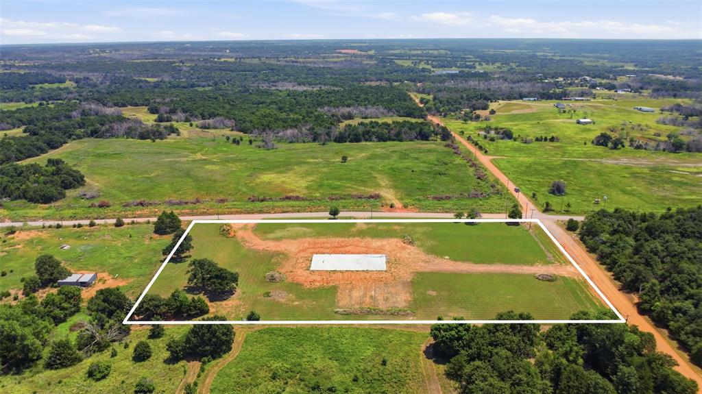 Expansive undeveloped lot featuring a gravel road frontage, established power poles, and green foliage