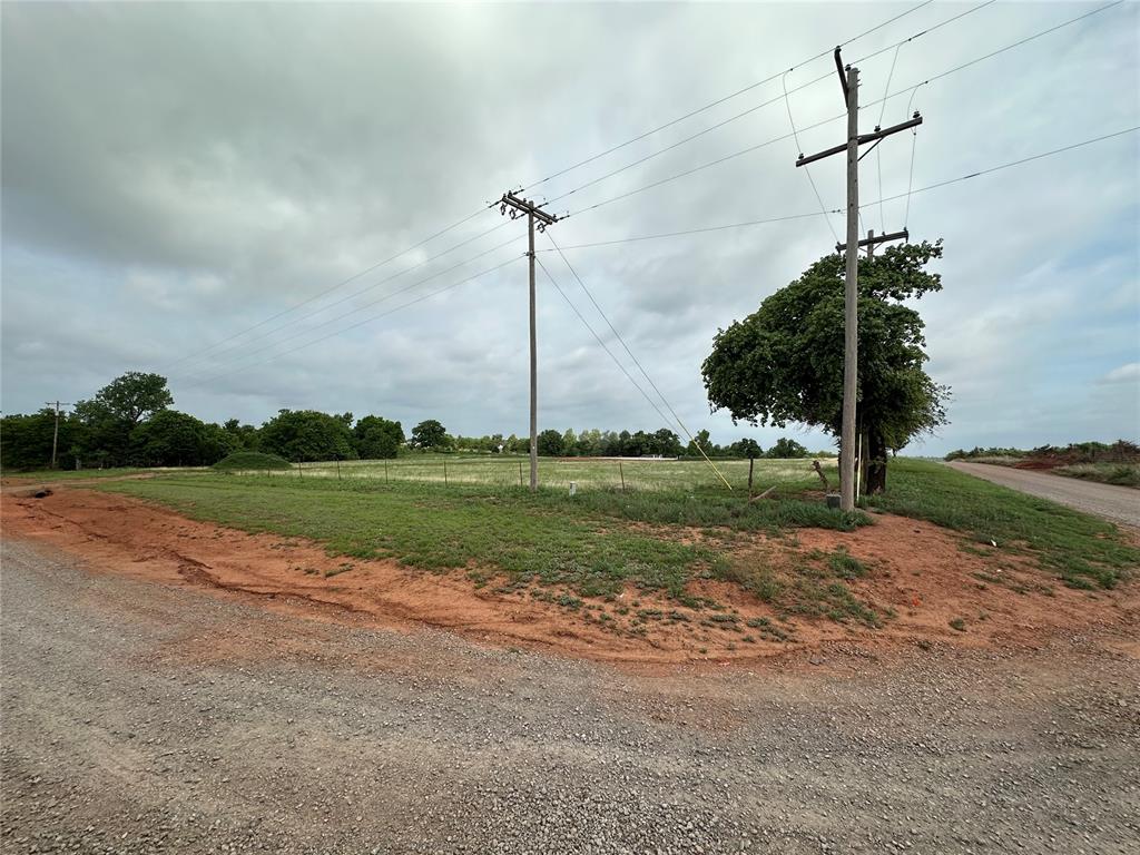 Expansive undeveloped lot featuring a gravel road frontage, established power poles, and green foliage