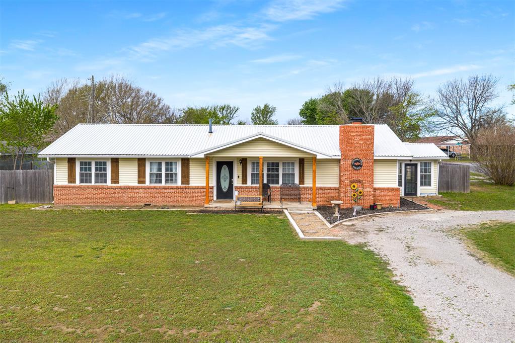 Single story home with a chimney, brick siding, gravel driveway, and covered porch
