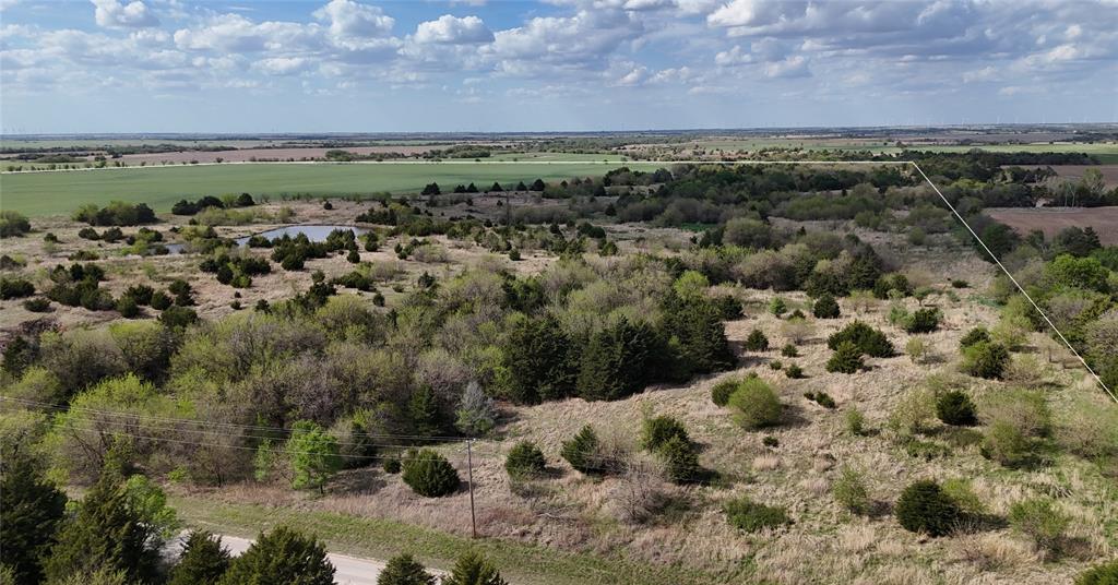 Expansive land offering with a visible pond and varied tree cover, bordered by open fields
