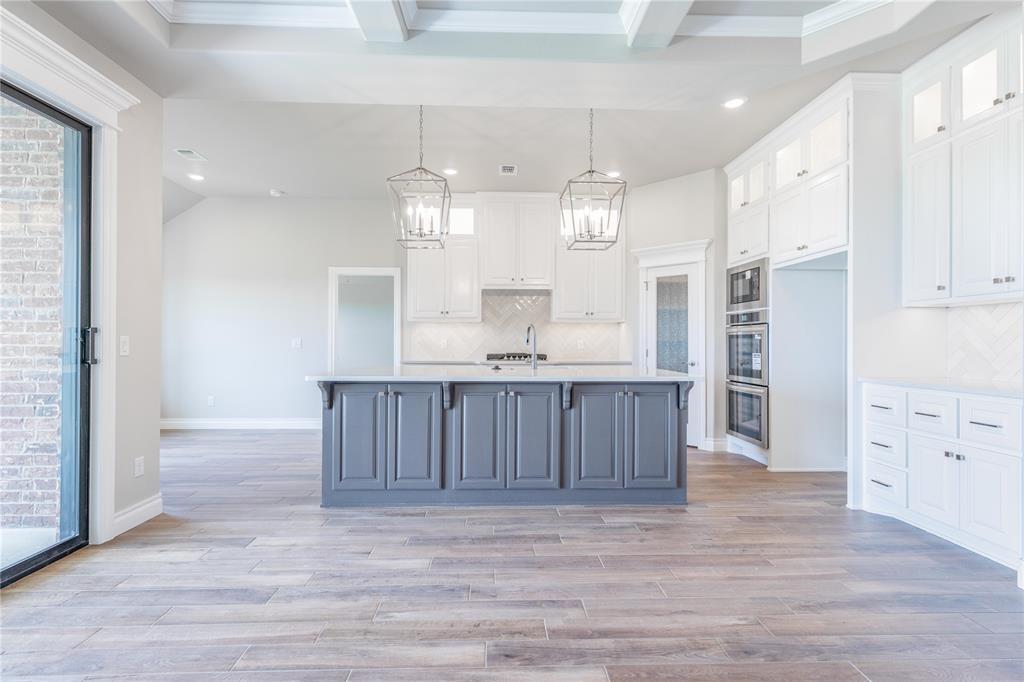 Kitchen featuring a large island with gray cabinetry, white perimeter cabinetry, wood-finish flooring, two hanging pendant lights, and stainless steel double ovens
