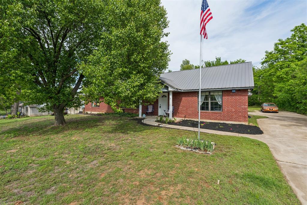 Brick exterior with a gray metal roof, featuring a covered front porch, a concrete walkway, and a landscaped garden bed with dark mulch