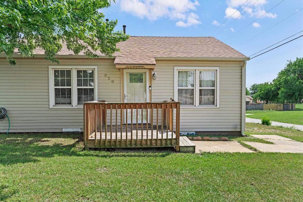 Siding exterior featuring a wooden front deck, a white entry door with glass pane, and a shingle roof