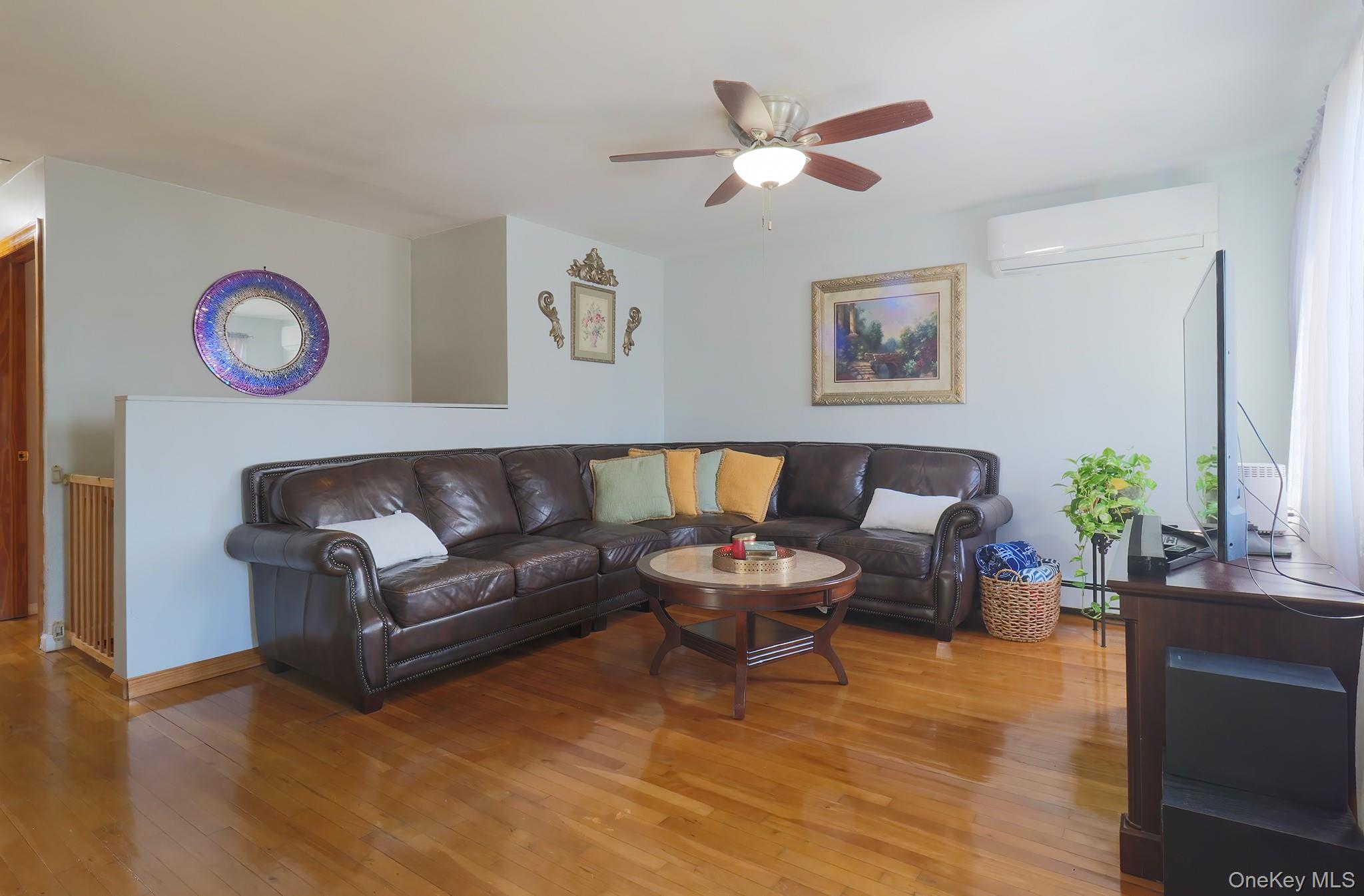Living room with hardwood / wood-style floors, radiator, ceiling fan, and a baseboard heating unit