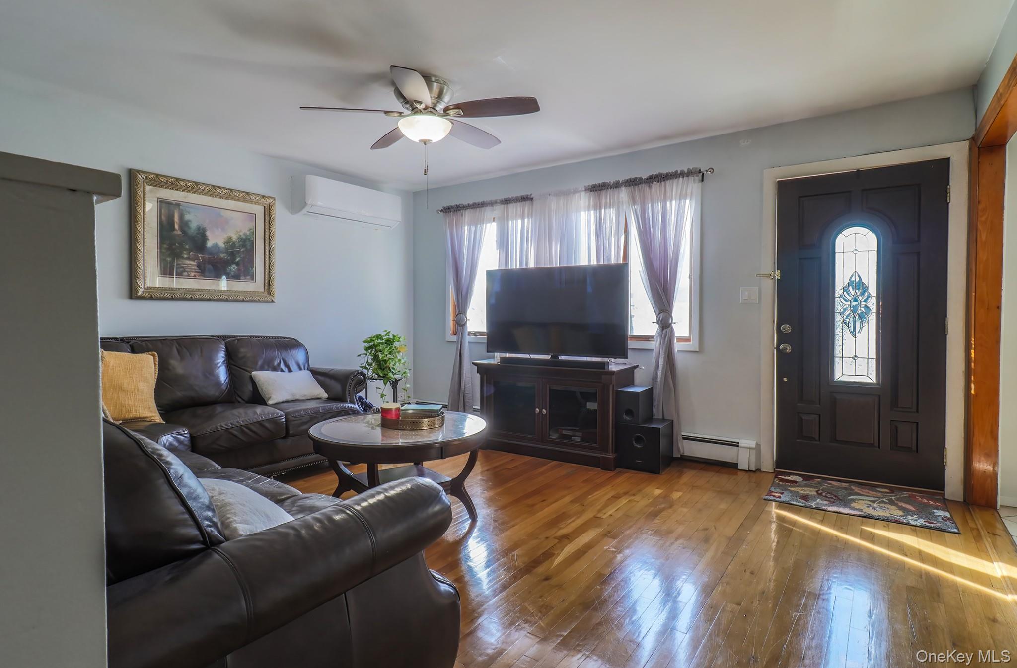 Living area with hardwood / wood-style floors, ceiling fan, and a baseboard heating unit