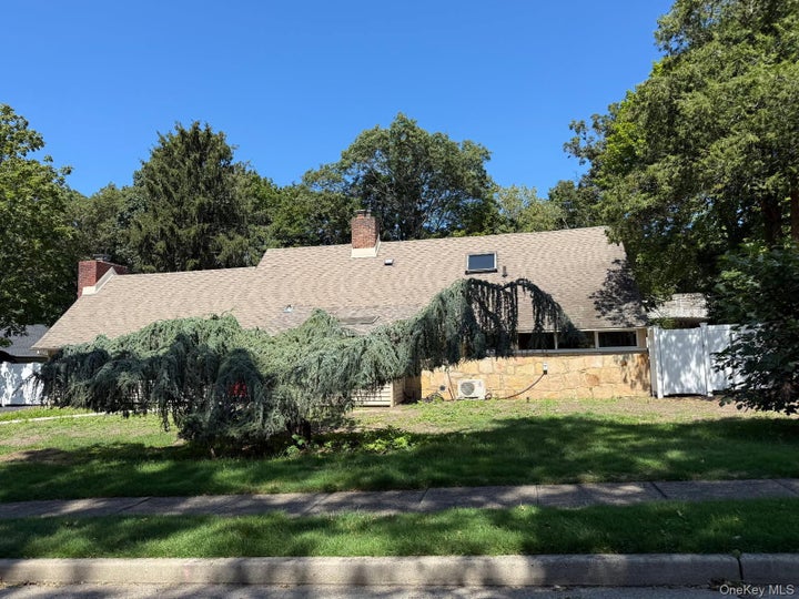 View of front facade with stone siding, a shingled roof, and a chimney