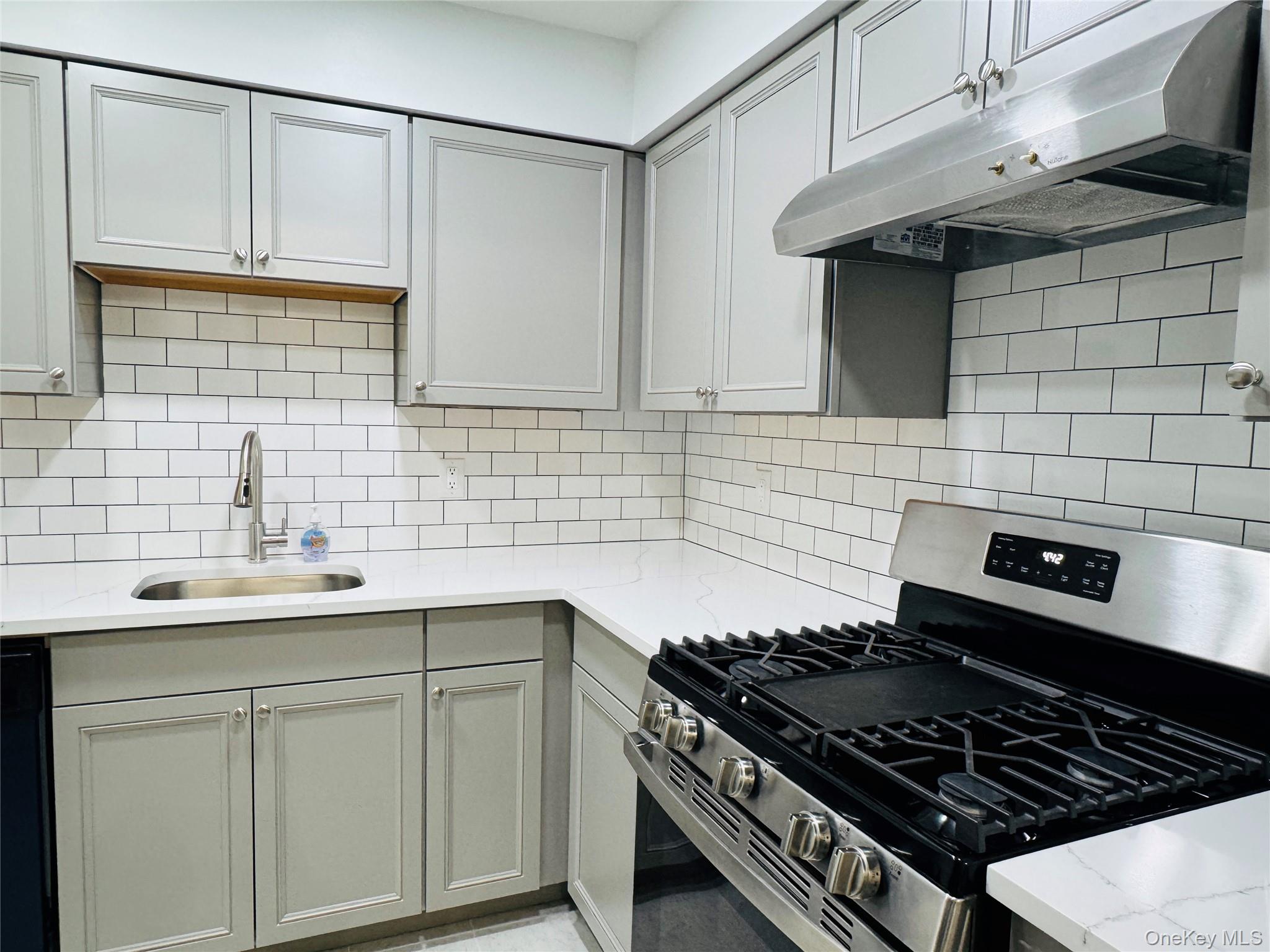 Modern kitchen featuring light gray cabinetry, white subway tile backsplash, white countertops, a stainless steel gas range, and a stainless steel sink with a gooseneck faucet