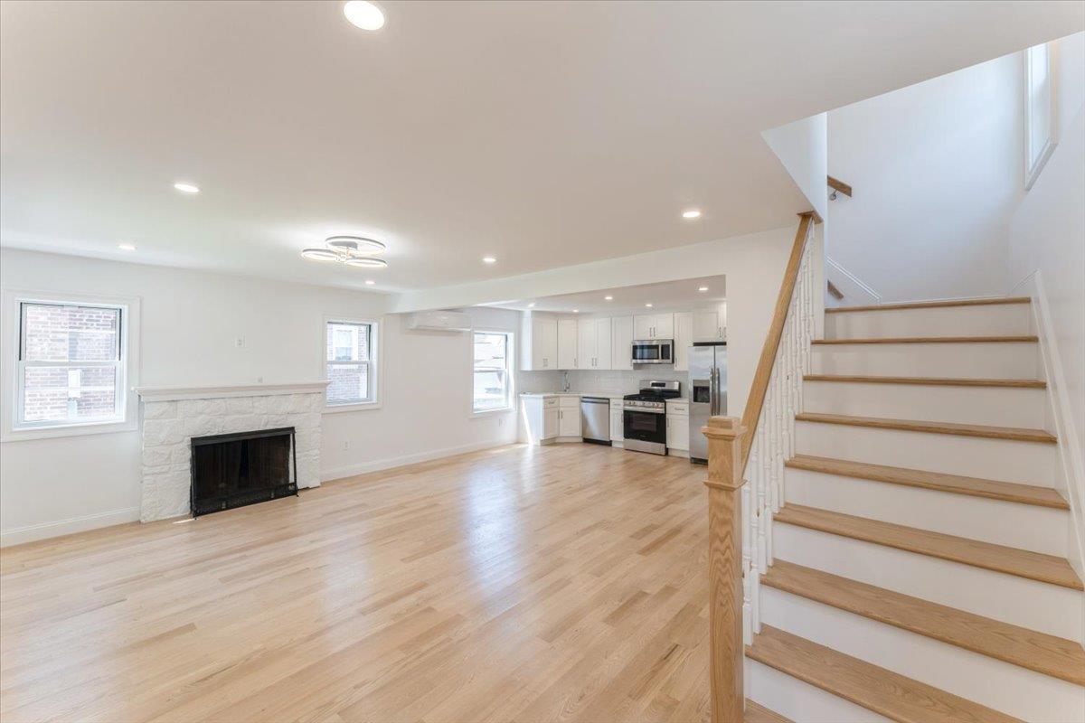 Unfurnished living room with stairway, light wood-style flooring, a wall unit AC, recessed lighting, and a fireplace