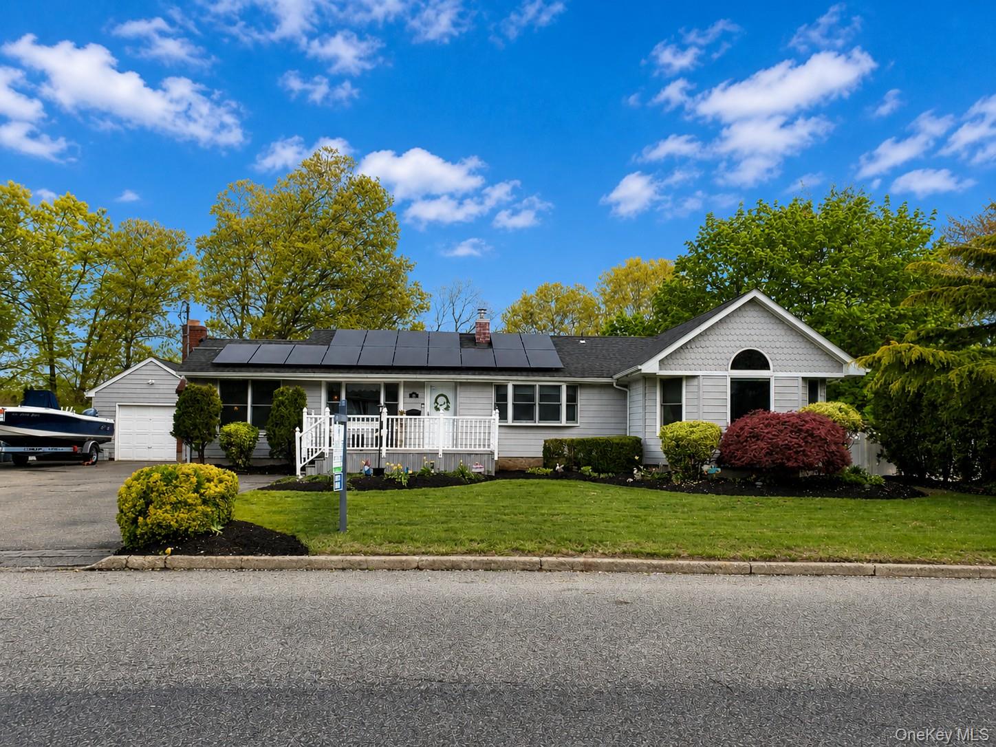 Single story home featuring roof mounted solar panels, a front yard, a chimney, covered porch, and driveway