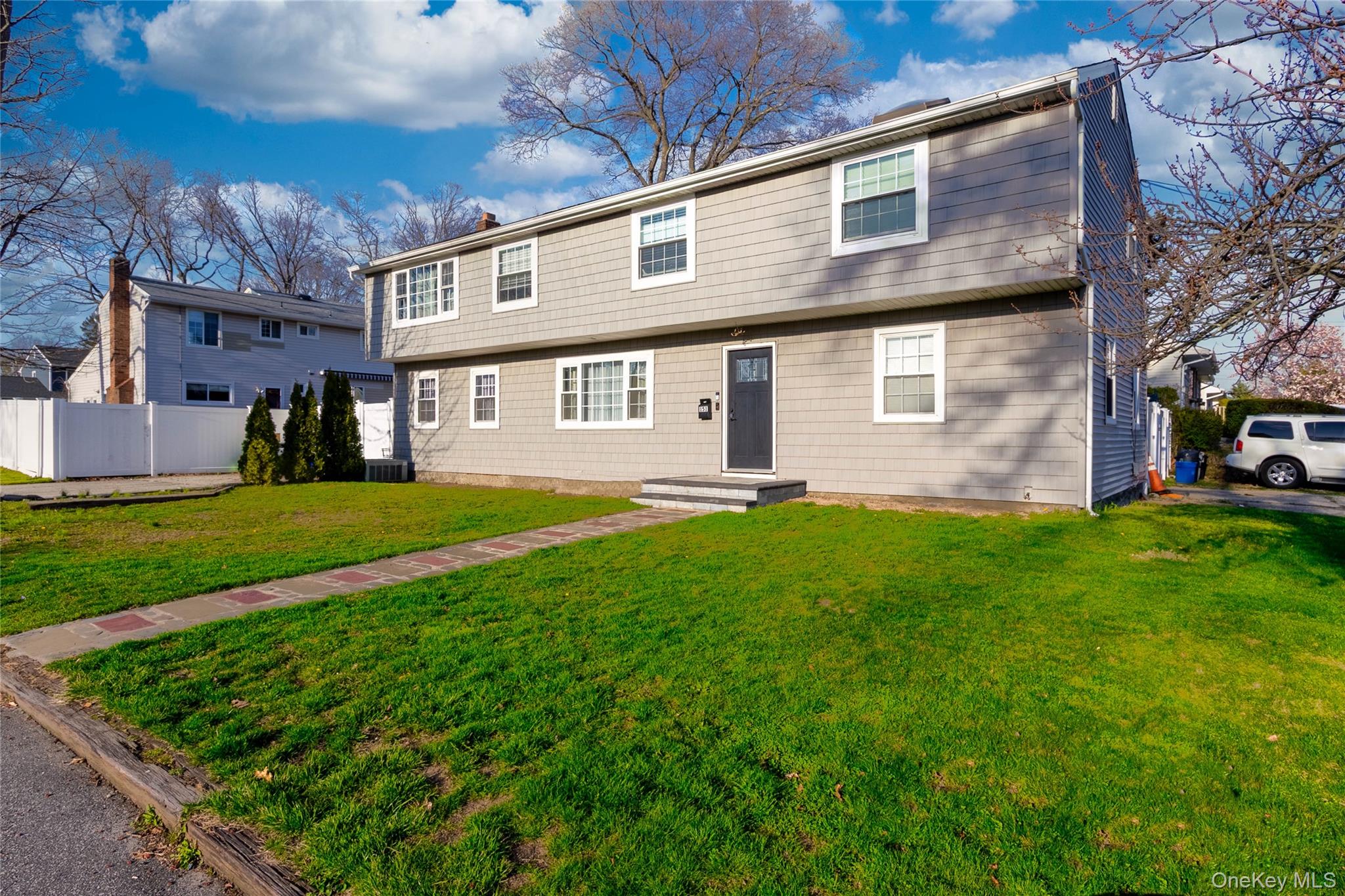 The property features a well-maintained lawn, a paved walkway leading to the front entrance, and a light gray exterior with white trim windows