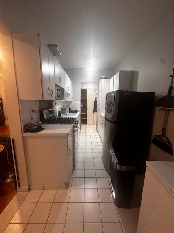 Kitchen with gas stove, freestanding refrigerator, light countertops, black microwave, and white cabinetry