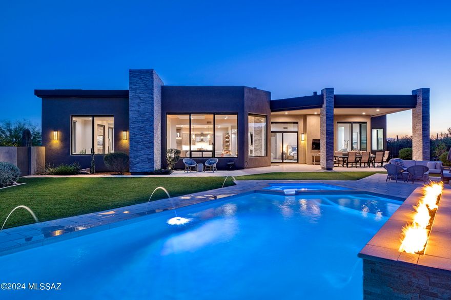 Located in the prestigious Pima Canyon Estates community, one of the finest private communities in the Southwest, and situated behind the secondary gates of Pima Gardens, sits a tranquil respite where one coexists harmoniously within the surroundings. The home's orientation offers soft natural light that filters into the great room through glass façades, with unobstructed Catalina Mountain and Pima Canyon views that stretch out over the surrounding desert landscapes. Entering the great room from the large glass front entry, one is immediately immersed within the dramatic mountain views while overlooking the pool and spa, providing a cinematic experience. Throughout the home, programmatic needs flow between indoor and outdoor living spaces that heighten the interior's sense of scale by extending the views outward.

The kitchen design features clean lines and a contemporary aesthetic, seamlessly blending into the surrounding architecture. Countertops offer a soothing natural stone finish, providing ample task space and adding to the kitchen's contemporary feel. Custom millwork, strategically placed for optimal functionality and ergonomic use, is positioned to overlook the great room, fostering a sense of connectivity within the living space. Tile floors line the interior, threading the living spaces together, while providing material continuity to the overall design aesthetic.

The generous owner's suite is privately sequestered on the north end of the residence, featuring an oversized walk-in dressing closet and luxuriously finished primary bath, which includes a large soaking tub, walk-in shower, and floating dual vanities. The balance of three secondary ensuite bedrooms are sequestered on the west wing of this split bedroom floor plan, perfectly suited for family, or guests alike.

Floor to ceiling glass walls spill out onto a back covered veranda, connecting the refuge of the home with the exterior living spaces. The pool and spa with linear fire element act as the centerpiece of the backyard, drawing in the surrounding mountain ranges, with the ever-changing skyline reflecting off the water's surface. Every comfort is considered and detail meticulously crafted, the result being an environment that offers a sense of ease to enjoy both lifestyle and entertainment.