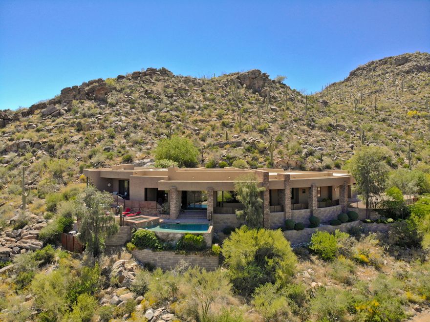 This gorgeous contemporary home in the sought after Canyon Pass neighborhood delivers some of the most scintillating views you'll find and from nearly every room in the house too. Relish the panoramic vistas of the Catalina Mountains, Tucson Mountains, the nearby rugged Tortolitas with its rocky, cactus strewn hillside, and in the evening take in the city light views of downtown Tucson! The home itself continues to deliver exceptional appeal with exquisite finishes such as travertine floors, Wolf appliances, and natural stone countertops. Each of the three guest rooms also offers it's own en suite bathroom. Also appreciate the built-in BBQ & spa outside, a 4-car garage w/ cooled storage room or workshop, separate office, and private rear yard. Further relax in the pool & spa outside!