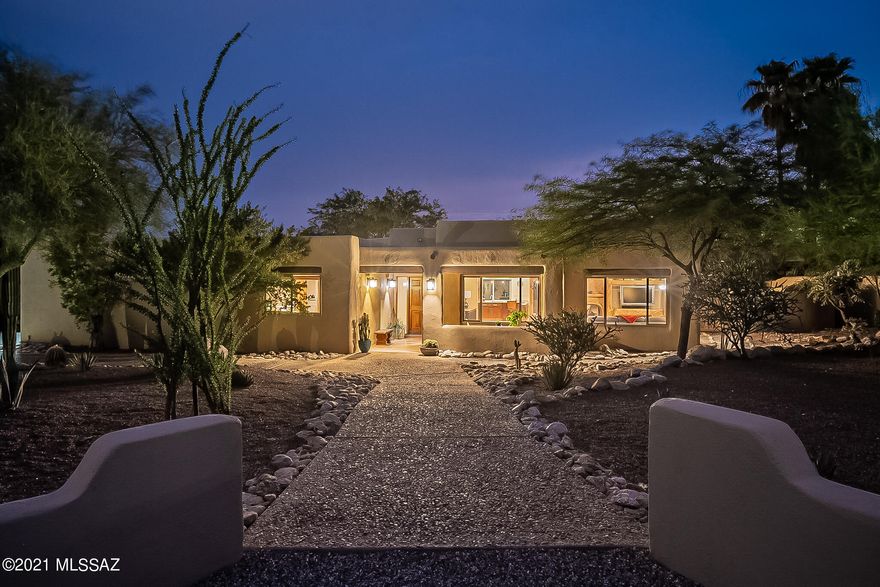 A Santa Fe style haven in Shadow Hills, with a fantastic open plan, a rare combination of feel and features, and a southwestern charm that instantly feels like home.  Its unique combo of space and layout can easily host the largest gathering without losing a bit of intimacy.  The light-filled great room soars, with viga/plank ceiling and an artfully painted three-sided fireplace that anchors the home without feeling imposing.  Thoughtfully designed and perfectly executed custom features at every turn.  Indoors and out, the space, flow, and ambience here are unmatched.  A huge primary bedroom suite, secondary BRs ideally situated for guests and office, without a single interior step...all enveloped by the verdant natural surrounds of Shadow Hills.  Full Vid & 3D virtual tour are a must-see. Not all square footage is created equal--just as not all "great rooms" are great--but there can be no question that, with a great room that earns every bit of its label, and with a rare combination of light, flow, space, all grounded with an easy, natural feel, this home lives larger than expected. 
There are so many thoughtfully added and well-done touches throughout, it's hard to know where to begin.  Starting in the great room, a wall of built-ins, with custom stained concrete countertop, a cabinet-door-faced wine fridge, and a bench window seat, allows for a buffet for serving holiday festivities or extra storage for the everyday (and a space large enough for multiple extra tables and seating).  Above, a beautiful viga and plank ceiling, with custom track spot lighting.  An impressively done three-sided fireplace provides centering point for the space, and a hub of warmth and energy during the "winter" months.  Though capable of burning wood logs, this wonder of a fireplace is plumbed with natural gas, as well, and is easily imagined as a center for winter-season warmth, family, and friends.  Across from the fireplace a custom wet bar, with an under-counter fridge of its own, bar-height seating at perfect conversation space from the kitchen, and plenty of storage for glassware and occasionals.  The kitchen, too, lives, works, and hosts bigger than what one would expect in a home of this size.  A U-shaped kitchen workspace, with gas cooktop, plenty of granite countertop surfaces, and open to the main living areas, is every bit a part of how this home lives, hosts, and plays so much larger and better than one would expect of a home of this size.  Accented by under-cabinet lights, the horizontally- arrayed backsplash is of hand-crafted glass tile, of a depth and intricacy that required a skilled specialist to install.
On the dining-space side of the kitchen, an outward-facing run of lower cabinets, with plenty of extra storage to make hosting easy and hassle-free.  An enormous picture window fills the space with light, perfectly sized to parallel a dining table.  
From the kitchen, the flow leads one past a well-situated wall of additional pantry cabinets toward bedrooms, perfectly laid out, with one bedroom split off to the eastern side of the home, and the second bedroom/office and primary bedroom suite on the south side.  The primary bedroom suite impresses, with a wall of built-in cabinetry for clothing storage, and recessed built-in shelving for artwork, photos, and deco pieces.  On the southwest side of the bedroom, a large window soaks the room in Autumn and Winter's afternoon light.  On the other, leading toward the en-suite bath with dual vanities, a well-appointed and high-ceilinged walk-in closet (outfitted with  shelving system from California Closets).  For convenience, the primary en-suite bathroom adjoins the laundry room (and through it, the hallway back to the kitchen), which allows for a circular flow and adding to the surprisingly spacious feel of the home, in both its appearance and function.
The third bedroom is perfectly set up to serve as home office or den, with its own southwest-oriented window to soak in cool-season light, green vistas, and desert blue skies.  In the left-most closet, a built-in shelving system (also from California Closets), and in the right?  A full-sized fold-down Murphy bed perfect for easy hosting overnight guests.  For the many who prioritize a home office, the easy-to-use bed allows this 3 Bedroom home to live more like a 4.  On the eastern side of the home, the second bedroom, with a window that welcomes the morning light and a generously sized closet as well.
Guests enjoy a spacious and well-renovated hallway bath, with italian marble tile floors, a glass-top basin sink, and a huge air-jet-equipped bathtub.

 It's been thoughtfully renovated over the years, with attention paid to detail and systems.  It should be noted that the three highest-cost replacements endemic to so many 35+ year old homes in the Foothills have already been taken care of here: the roof has been replaced and re-worked to prevent ponding, the HVAC replaced with a Trane system, and all of the windows in the home replaced with Milgard dual-paned windows with work done by Olander's.  The water heater was replaced in 2021.  The concrete floors throughout the living areas, too, have just been refinished in August 2021 (after listing photos were taken).  

While all of those features are enough to fall in love with, the outdoor living spaces are superb in their own right.  In front, an east-facing courtyard and intimate covered patio, perfectly sized for a cafe table, a cup of coffee, and enjoying the sun rising over the desert natives (ocotillo, agave, and a massive multi-armed saguaro).  On its tree-shaded western side, the home opens at three points to the covered patio and the privacy and lush natural beauty of a low-walled back garden.  The border between this back yard/patio and natural desert is just well-defined enough, with a low wall that sets the interior managed space apart from the wild half, without blocking the energy and wonder of the natural area beyond it.  With just the right amount of shade from Palo verde and Mesquite, an expansive flagstone-surfaced area allows for multiple areas to sit and host, whether for outdoor dining or around the outdoor firepit.  Under the rich viga and planked porch roof, a built-in stainless steel gas grill, and plenty of room for sofas AND for tables and seating atop the freshly painted surface.  The convenient laundry-area door comes into play here, too, as a natural path for guests to transit to the hallway restroom without having to navigate the kitchen.  

With pathways that lead through gates on either side of the home, there's a generous feeling of space and flow all around. 
A perfect blend of natural aesthetics, beautiful surrounds, and feature-rich interior spaces that have been renovated and outfitted to maximize enjoyment, this home stands apart from the rest.  And set as it is in the heart of one of Tucson's most coveted neighborhoods, it will no doubt prove a treasure for whomever is lucky enough to call it "home."