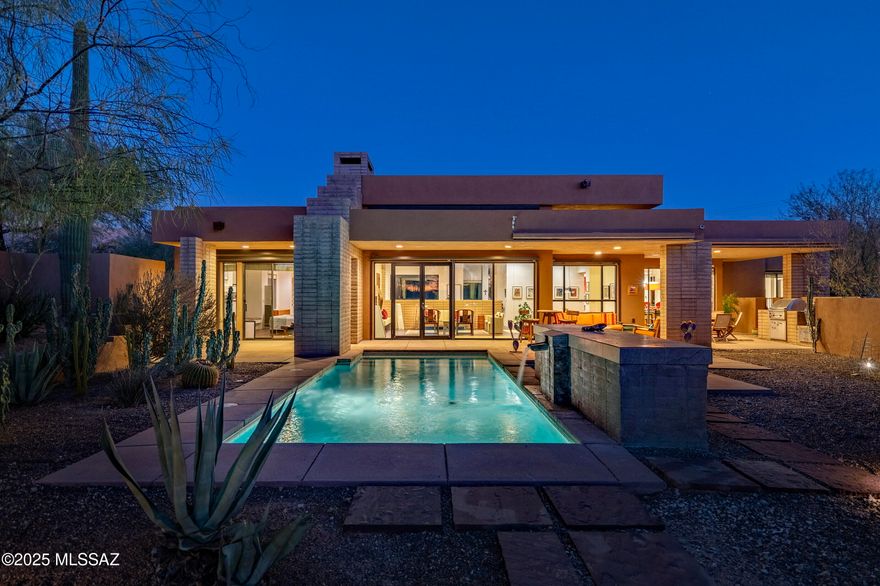 Nestled within the heart of the Catalina Foothills, this Kevin Howard design emerges as a quiet retreat emphasizing simplicity, calmness, and the harmony of space and light, where the architecture integrates seamlessly within its natural surroundings. Designed to embrace the essence of the desert landscape, the residence is thoughtfully oriented to capture soft, filtered natural light, which pours into the great room through expansive glass façades. From the moment you step through the glass entry, you are immersed into a cinematic experience that unfolds as the evening sunset casts dramatically over the pool and spa, grounding the home in its setting. The residence flows effortlessly between interior and exterior spaces, blurring boundaries and extending the scale of the home outward. Each programmatic element is meticulously considered to heighten the experience of living within the Tucson desert lifestyle.

The kitchen, a centerpiece of functionality and design, reflects clean contemporary lines that echo the home's design language. Smooth natural stone countertops offer both beauty and practicality, while custom rift oak millwork integrates seamlessly, creating a warm yet modern aesthetic. Positioned to flank the great room, the kitchen becomes a space of connectivity, bringing people together while maintaining an understated elegance. Tile flooring extends throughout the interior, creating visual and material continuity that unifies the design. The owner's suite, located in its own private wing on the north end of the residence, is a retreat unto itself. Featuring a walk-in dressing closet and a spa-inspired bath with a large soaking tub, walk-in shower, and floating dual vanities. On the opposite end of the residence, two generously proportioned secondary en-suites provide comfort and privacy for family or guests, creating a thoughtful split bedroom floor plan.

Floor-to-ceiling glass walls open onto a covered veranda, seamlessly connecting the home's interior refuge with its exterior living spaces. The backyard, anchored by a pool and spa, becomes a focal point for reflection as the water mirrors the ever-changing desert skyline. Every detail of the home has been crafted with precision and purpose, resulting in a space that exudes ease and elegance, offering both a lifestyle of comfort and a venue for unforgettable moments of connection and celebration.