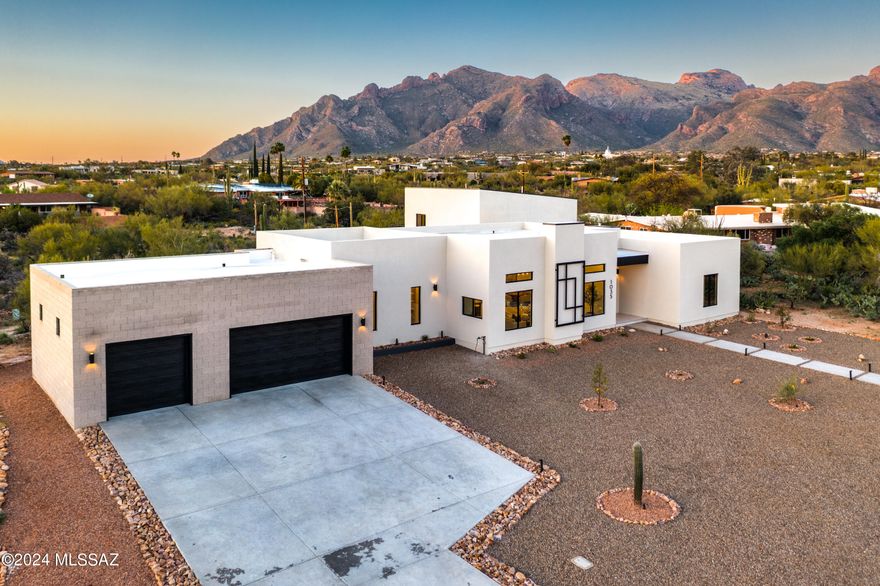 Presenting a modern residence nestled in the highly sought-after Santa Catalina Estates, now available in 85718. Originally constructed in 1964, this home underwent a complete transformation just finished in 2024, emerging as a contemporary rebuild from the original slab up, boasting 3,988 square feet of living space. 

Step inside through the grand front iron pivot door into an inviting open-concept layout, accentuated by soaring 12-foot ceilings. The distinctive bloque exterior of the garage and interior wall in the primary bedroom and bathroom adds to the residence's contemporary aesthetic. Featuring five bedrooms, three bathrooms, and two half bathrooms, with the 5th bedroom offering flexibility as a hobby room with a deep storage closet. The primary suite, with an impressive 20-foot ceiling, complete with balcony and slider doors that offer picturesque mountain vistas, also boasts a 613-square-foot loft space. Ascend the metal and wood stairs, leading to your private loft area, ideal for a gym, office, or relaxation space. The primary bedroom also includes two walk-in closets, dual sinks, a freestanding tub, walk-in shower, and a private balcony offering mountain and sunset views.

The kitchen impresses with custom-built walnut wood front cabinets, a sizable island, waterfall quartz countertops, and top-of-the-line GE Cafe stainless steel appliances, including a gas stove and pot filler faucet. The walk-in pantry provides ample storage, while the adjacent bar area features a wine cooler, glass lighted wine closet, and a window with sunset views, perfect for entertaining guests. Additional highlights include a three-car garage with insulated doors and a side mount door opener, hardwired for an EV station inside, along with ample driveway parking.

Outside, the expansive patio area features covered patios, a newly installed pool with a baja shelf, lush greenery, an exterior shower, and a convenient half bathroom. Also featuring an irrigation system, synthetic grass, and desert landscaping for easy maintenance.
