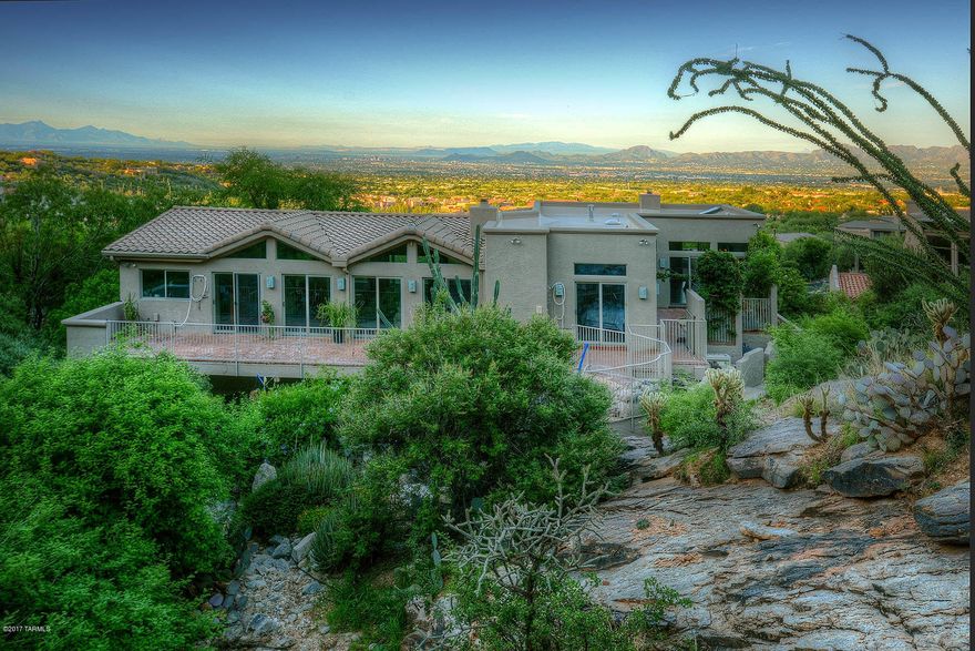 High behind the gates of Sin Vacas you find this home literally nestled in the heart of the Catalinas sitting on 21.56 acres as its backdrop. Make your way to a private driveway lined with mature natural vegetation of high country desert. Upon entering you may visit a private master suite on the first floor, just ideal for visiting guests. Then, depending on your preference, take the brick lined stair well or the elevator to the second floor where you will find a second bedroom & another master bedroom w/fireplace & spectacular mountain & city views. On this second floor we find the living room & dining room in a great room setting spanning & hydrologist inspired steel bridge over the canyon wash. Come visit & commune with nature at every turn. Borders Pusch Ridge wilderness area.