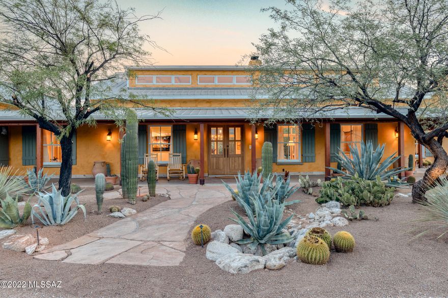 Welcome to Marigold Ranch, a one-of-a-kind property perfectly resting in the
exclusive Tanque Verde Valley.
As you approach this home, your eyes are delighted by the true essence of this
Southern Arizona masterpiece. As Shakespeare is to literature, this home is to
luxury in every aspect. Fashioned after historic, sprawling Texas ranches,
Marigold features a wrap-around porch that brings the desert to your toes.
This home was built with solid block construction walls featuring E-Crete, an
energy-efficient aerated concrete system. The resulting thick exterior walls are
finished with stucco and a natural pigment lime wash, giving a sunny golden-hue
to the exterior. A pitched standing-seam steel roof reminiscent of old ranch
buildings sheds seasonal rains into planting areas around Clerestory windows near the entrance bring more daylight into the interior, along with perimeter upper transom windows and three sets of French doors on the north side. Double-hung windows framed by sage green shutters lend a classic, timeless look to the exterior.

The residence was carefully sited on the three-and-a-half-acre property to avoid disturbing the numerous saguaros and to best-capture the mountain views to the north and east. The grounds are meticulously xeriscaped with unique plantings, relics and sculptures.

Custom Douglas fir double doors greet you as you enter Marigold Ranch and the spectacular floor-to-ceiling double-sided fireplace commands immediate attention. Framed by breathtaking views of the Santa Catalina mountains, this fireplace's style, scale, and charm was inspired by the one in the reading library at the Arizona Inn, a 1930s Spanish Colonial Revival hotel near downtown Tucson. Another prominent feature of the living room area is the set of vintage wooden doors reclaimed from the Tucson Icehouse (circa 1920) that contains the recessed entertainment system. These beautiful features honor our local history with authenticity and anchor the dwelling in Tucson's past.

The craftsmanship of this unique property is showcased through the exposed rough-hewn ceilings and structural beams, which are connected by hand-forged steel bracketry, barrio-style walls, and the solid Montana white pine flooring. The architectural design and flow of the home capture a sense of true peace and tranquility.

The walls feature white hand-troweled diamond plaster, keeping the interior fresh and light. The home has four natural gas fireplaces, creating a wonderfully warm, inviting ambiance - adding comfort to our desert winters. In September 2022, three new HVAC units were installed to keep the house comfortable all year round.

The open kitchen features a tile-clad backsplash with a custom cement range hood, white Calcutta marble across all surfaces - including a Douglas fir island, side pantry, and breakfast nook highlighted with white cabinetry throughout. From the kitchen, one can take their favorite book and a warm beverage to the screened-in porch area to enjoy the morning sunrise.

A wing containing a study and the primary suite angles off one side of the great room, creating a protected courtyard for the north-facing pool terrace. On the opposite side of the great room, another wing includes two guest suites with access to nature's outdoor garden.

Inside and out, this fully furnished and decorated home is filled with many special touches. A mix of contemporary and traditional furnishings and accessories celebrate the colors of the desert and emphasize comfort. The home has two deep Ralph Lauren Home sofas, covered in a hay-colored Manuel Canvas fabric, matching alder-wood low table and sofa bookcase built by local furniture maker Marc Perry, and duck cloth slipcovered armchairs to
anchor the living area.

The pale desert colors of the furnishings and fabrics keep the emphasis on the art. Decorative arts collections, including an assortment of Navajo rugs, antique Indian baskets and pottery, as well as western paintings by California artist Dennis Ziemienski, glasswork by Tom Philibund, and many others, adorn the long
hallways, shelves, and surfaces between the great room and the wings to the east and west.

The thoughtful planning, tasteful eclectic décor, and light-filled layout make this an extremely livable home. Welcome home to Marigold Ranch.