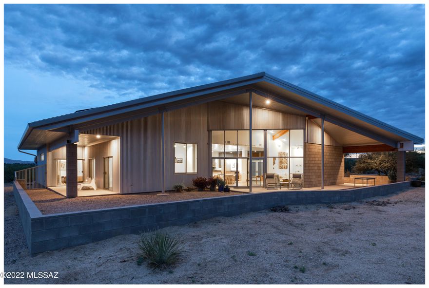 Raincatcher, designed and built by Tucson Architect Kathryn McGuire, was completed in 2018. The home, adjacent to Catalina State Park, provides a panorama of the Santa Catalina Mountains.
 
The 4 bedroom, 3 bathroom, 2,668 Sq Ft home incorporates regional design influences with modern architecture. Offered with the entire 4.5 acre natural desert site, the home was strategically placed to maximize views, privacy and efficiency.

The drive to the property starts at the mail-box cluster on Lago del Oro Parkway, just past the Miraval Resort and Spa. Gently rolling along the country road passing local flora and fauna, one can recall a favorite country road song, producing a decompression of the day, and heading towards a home that provides respite. A beautiful gate opens to a welcoming arrival past the proud cistern, a celebration of the rainwater collection. An intimate north patio leads into the open entry, easy-flowing areas, and the heart of the house. Large windows, with the protection of covered patios, provide magnificent views from every room in the house.

Construction began in 2017 with the intent to maximize views and natural light and ventilation. Inspiration came from agrarian barns with simple forms and the low maintenance of metal, glass, and masonry. The goal to have a sustainable building in the desert contributes to the materiality and the methodology of the work. The 8" thick post-tensioned polished concrete floor, steel columns and a well-insulated double-wall framed construction supports a substantial truss system, ideal for passively maintaining a cooler building. The intention to have a solar power system and rainwater collection determined the application of the sloping big metal roof, with gutters diverting rainwater into a 16,000-gallon storage tank connected to a 3-stage filtration system. The house has the potential of being a self-sustainable dwelling.

Although the location is not far from communal amenities, it feels remote and comfortable in the desert and mountain surroundings, a place to enjoy the activity of numerous birds and Tucson's spectacular rainstorms and sunsets.
 
For those seeking a truly remarkable home with architectural provenance and integrity, Raincatcher offers something completely unique and authentic.

FEATURES:

* 4 BEDROOMS, 3 FULL BATHS, 2 CAR GARAGE WITH STORAGE AND ATTIC ACCESS (ALL INSULATED)

* ENTER INTO A SPACIOUS WELCOME AND A FULL INTRODUCTION TO THE CATALINA MOUNTAINS. OPEN LIVING AND DINING AREA PROVIDES THE MOST FLEXIBLE USES OF SPACE AND NATURAL LIGHT, WITH CONTINUOUS ENJOYMENT OF THE NATURAL DESERT ENVIRONMENT

* FLOORS ARE POLISHED NATURAL CONCRETE 8" THICK POST-TENSIONED

* ROOF: R-VALUE 45+ CORRUGATED METAL ON LARGE TRUSS SYSTEM SLOPED FOR BEST ANGLE FOR SOLAR PANELS AND RAINWATER COLLECTION. ATTIC SYSTEM FOR SOME STORAGE AND EFFICIENT LOCATIONS OF DUCTWORK AND LINEWORK FOR ELECTRIC AND WATER IN INSULATED ATTIC ENCLOSURE

* WINDOWS ARE LOW MAINTENANCE METAL FRAMES WITH THERMAL BREAKS AND HIGH EFFICIENCY, LOW-E DOUBLE GLAZED U-51.

* 30 SOLAR COLLECTION PANELS, 8.85KW SYSTEM INSTALLED BY TECHNICIANS FOR SUSTAINABILITY JUNE 2017

* WATER: A WELL IS SHARED BY 5 PARCELS AND IS LOCATED 330 FEET WEST OF THIS SITE.

* THE 16,000 GALLON RAINWATER COLLECTION SYSTEM WAS COMPLETED IN JANUARY 2021 BY ECOSENSE AND MARK RAGEL, PROVIDING A NATURALLY SOFT AND PURE WATER SYSTEM FOR THE ENTIRE HOUSE

ABOUT THE ARCHITECT:

Kathryn McGuire is an architect practicing in Southern Arizona. She is also co-author of the book Powerhouse: The Life and Work of Judith Chafee, published by Princeton Architectural Press. Educational experiences took her from Philadelphia, to Tucson, and Hawaii, learning about regional considerations for sustainability. She chose to return to Tucson to complete her architectural studies and work within the professional field. At first she was a student, then an employee and friend of Judith Chafee (1932-1998) for over twenty years. Starting as an intern, then project manager and associate, McGuire worked with clients, engineers, and other advisors. The work was challenging as Chafee's work responded to various clients' and environmental needs. McGuire's own practice is still based on many of the principles experienced in the Chafee studio, dedicated to desert adapted building strategies and regional modern architecture.