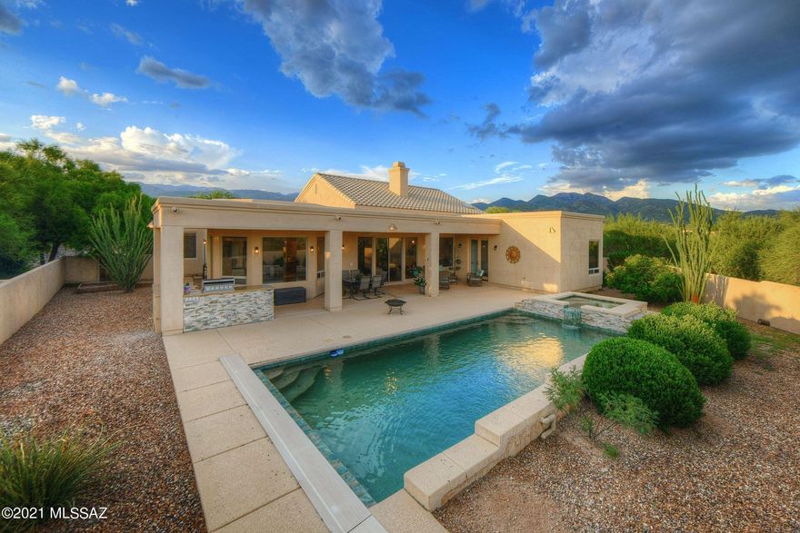 Seller to entertain/counter offers between $850k-$900k. Showcasing scenic mountain views and exceptional privacy, this inviting home is quietly nestled on a gorgeous acre lot surrounded by
lush natural desert. Located at the end of a cul-de-sac in a small, gated enclave of homes, enjoy
serene living near Redington Pass in Northeast Tucson. A tranquil backyard retreat features a
resort-like pool and spa with stacked stone custom water features, an expansive covered patio, and handsome outdoor kitchen that will make outdoor entertaining a breeze! Inside, the home is brimming with beautiful finishes throughout, including stylish wood plank porcelain tile, recessed lighting, bathroom updates, cozy fireplace and built-ins, as well as a deluxe laundry room loaded with storage and workspace th is sure to please. The home's updated kitchen is designed with plenty of counter and cooking space, featuring a large island for serving and socializing. White cabinets brighten up the area and a luxe stainless steel farmhouse sink is a showstopper. Other features include a sleek custom backsplash, Bosch appliances, wall ovens, and a 5-burner gas cooktop. Bright, open living spaces are generously sized, including a central great room, as well as formal living and dining. Gracious owner's suite with private backyard
entry, large walk-in closet, and a lavish ensuite bath. Two additional bedrooms share a Jack-and-Jill bath, and a fourth oversized bedroom offers plenty of space for guests, a family office, hobbies, or home gym. An in-home Bose sound system, four-car heated/cooled garage, and stunning brick paver driveway with charming entry courtyard take this home to the next level!