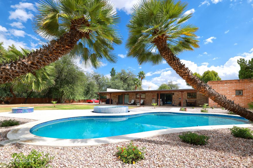 Nestled within the serene confines of Forty Niners Country Club Estates in Tucson, Arizona, rests a timeless masterpiece that seamlessly marries classic burnt adobe charm with modern comfort. set upon a picturesque 3/4 acre lot adorned with majestic, mature trees, this residence exudes a sense of tranquility and natural beauty. The exterior of the home embodies the quintessential Southwestern aesthetic, with its burnt adobe construction. As you step inside, you are greeted by a sense of warmth and authenticity, with the interior spaces updated to harmonize with contemporary lifestyles while preserving the integrity of the homes historic character. The Mexican tile Archways provide a sense of solidity and timelessness, while strategically placed windows invite in abundant natural light and frame views of the lush outdoor landscape with color changing fire pit and crystal clear pool & spa, completely surrounded with Cool Deck, RV and Boat Accessible; Plumbed for full outdoor shower. Property boasts a full 12'x16' storage shed. The heart of the home is the spacious living area, featuring exposed wooden beams, 2 charming gas fireplaces with glass stone and handcrafted details that showcase the craftsmanship of the home's construction. This inviting space serves as the perfect fathering spot for family and friends, with ample room for relaxation and entertaining. The gourmet kitchen is a chef's delight, blending modern amenities with rustic elegance granite countertops and high-end appliances provide both style and functionality, while the breakfast bar offers a delightful spot to enjoy, morning coffee while taking in views of the backyard oasis. The home boasts multiple bedrooms and baths, each thoughtfully designed to offer comfort privacy. The master suite is a luxurious retreat, featuring his and her walk in closet and Roman Shower. Outside the expansive grounds beckon you to unwind and explore. Towering mesquite trees provide shade and privacy, creating a tranquil sanctuary amidst the desert landscape. A covered patio offers an ideal setting for outdoor entertaining while a sparkling pool and spa provide a refreshing respite from the Arizona Sun. With its harmonious blend of classic burnt adobe architecture modern amenities and idyllic natural surroundings, this home offers a rare opportunity to experience the timeless allure of Tucson Forty Niners Country Club Estates.