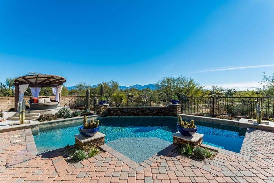 Exquisite home on premium view lot - lovely Catalina Mountain views - abutting natural desert. This is a very private home with 2 masters & a guest bedroom- all w/en suite bathrooms. 2nd master is actually a full guest quarter suite w/private living room are & bedroom & alcove office area - room has connections for W&D if desired. Many dining areas: formal dining room, breakfast nook & very spacious island breakfast bar.  Separate office (w/fabulous views) & powder room near kitchen. Grand great room concept floor plan. 3 car tandem extended (4ft) garage. A grand professionally designed backyard boasts a salt water pool w/2 waterfalls & SunX solar heating system, custom Cabana - stylish, relaxing - iron fie pit w/glass stones, expansive brick pavers.  All rooms have upgraded fans/lighting. Additional special features include: custom designed security system w/front door camera, surround sound system & external patio speakers, arch entrances inside home, arches metal front door w/opening glass insert, extra outlets throughout, whole house water softener, Butlers pantry cabinet area w/glass doors, laundry room w/built-in utility sink & folding station & abundant storage. Massive master bedroom suite is extended, w/stylish custom closet w/passage to laundry room - along w/exquisite shower & large soaking tub. Gourmet kitchen highlights include slide out drawers, staggered height cabinets, corner unit glass, stainless steel GE Profile appliances: 5 burner gas stove, in wall double oven, in wall microwave, French door refrigerator w/ice & water dispenser.  This is a lovely, immaculate, multi-generational home with a spectacular custom backyard entertaining area. Flow from great room & kitchen through the massive door that partially closes toward wall. Spectacular entertainers home.  Most of furnishings are available on separate bill of sale.