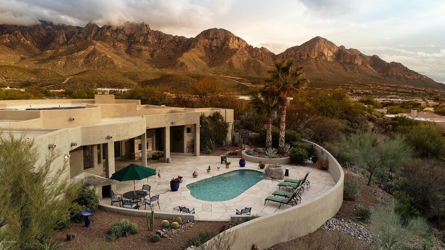 Architecturally stunning, drop dead views of Pusch Ridge, gorgeous high-end finishes, lovely pool with waterfall in a beautiful rear yard, broad covered terraces...located in very private gated Palisades Point Estates....and now available for discriminating homeseekers. Set on a hill with sweeping views of landmark Pusch Ridge and the Catalina Mountains from most of the home as it curves graciously around the large property situated at the end of a quiet cul-de-sac, this elegantly contemporary home can be enjoyed equally by families and retirees. Its features are classic and enduring: travertine and slate floors, 3 handsome fireplaces, coffered ceilings in multiple spaces (remember to look up!), wall of windows, graciously curving terraces and generous living spaces provide a backdrop for comfortable yet elegant living. Art niches are abundant throughout the home. The living and dining rooms enjoy curved walls of windows showcasing the magnificent views, and sliding glass doors leading to the front covered terrace sweeping across the entire front of the home, providing generous spaces to entertain or just relax and enjoy the dramatic sunsets and sunrises. The large kitchen has richly shaded black granite counters curving dramatically around the space, accented by stainless appliances and handsome wood cabinets. The person washing dishes may be distracted by the incredible views across the living room to the Catalinas. A breakfast area overlooks the pool and waterfall in one direction and those fabulous Pusch Ridge views in the other direction; a fantastic spot for your morning coffee or evening supper (if not outside!). The master bedroom enjoys views also in both directions, with sliding glass doors providing access to the front terrace on one side and the lovely rear terrace, pool and gardens on the other side. A fireplace in the corner adds yet more warmth. In the large-enough-for-a -small-party master bath area, the setting is one of gracious order with a large cabinet separating the double sinks set in handsome granite. A Jacuzzi tub is set into an elegant travertine surround and has its own coffered ceiling, while the walk-in shower includes a convenient bench. The walk-in closet includes a built-in dresser with drawers. On the other side of this stunning home are three additional large bedrooms and a den, all with views of the pool and surrounding mountains; one bedroom is currently being used as an office with handsome built-in desk and cabinetry. The den functions as a sitting room for the remaining two bedrooms. A lovely powder room has an attractive vessel sink. A large laundry room and additional wall of storage in the 3 car garage complete the interior spaces. Stepping out to the rear of this fabulous home, the entire area is floored in attractive flagstone slabs. Raised garden beds are filled with lush desert landscaping. The pool, with solar heat, is of a comfortable size and is perfectly accented by a dramatic rock waterfall. A covered patio area enjoys a handsome gas fireplace with banco seating that creates a warm and inviting spot to gather. And note the built-in misting system for those hot summer evenings, a perfect touch. This home is truly a class act, and you are invited to call for your private showing.