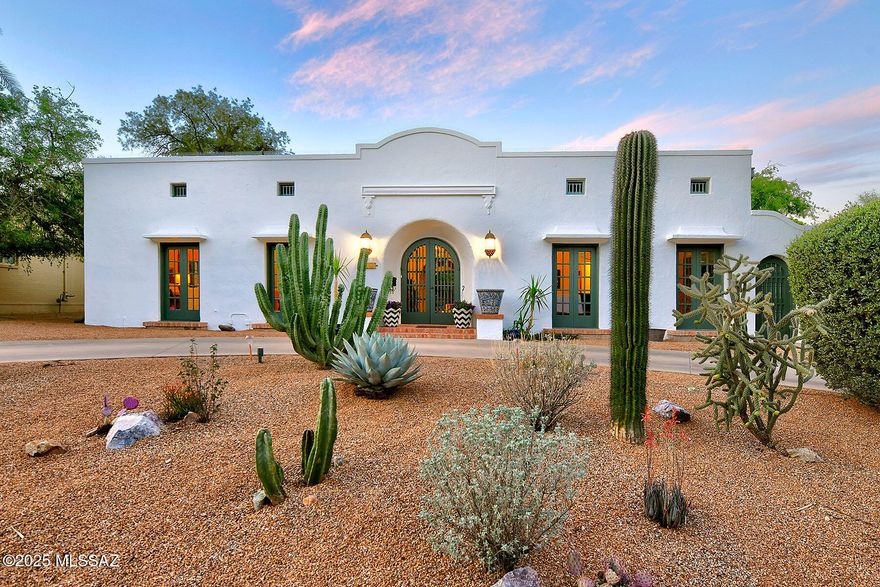 In the highly coveted enclave of Sam Hughes, within the storied University Manor, stands a singular gem — a 1932 Spanish Revival residence of exceptional character and presence, a short walk to the UofA campus and sports complex. With its commanding street appeal and timeless architecture, this home is a rare confluence of history, elegance, and artistry.  Enter through a dramatic zaguan to discover interiors graced with 10' to 12' ceilings, original scored integral-colored concrete, rich brick, warm wood, and timeless flagstone floors. French doors, along with arched windows and doorways, cast dappled light throughout the home, enhancing its romantic charm.
The beautifully renovated kitchen is both functional and full of soul, featuring a 6-burner stove, double ovens, cozy eat-in nook, and clerestory windows that bathe the space in natural light.
An expansive living room boasts a stately fireplace and custom built-in library, while the formal dining room offers refined entertaining with a distinctive hanging buffet. Beyond an arcaded breezeway, a separate family room with soaring beamed ceilings stands at the center of the home. Enhanced by a renowned Tucson Architect, Ned Nelson, it showcases the Artisan's dramatic fireplace and hearth, facing a terrarium.
The primary suite offers a serene retreat with a vintage ensuite bath. A second bedroom enjoys access to a hall bathroom, while a third bedroom suite features its own private, recently renovated bath, ideal for guests or multi-generational living.
Freshly painted inside and out, the home is surrounded by lush, mature landscaping. Adobe walls and ocotillo fencing lend privacy to a backyard sanctuary featuring fruit trees, a tranquil water feature with pond, a covered patio with new concrete overlay, and a glistening pool with a brand-new pump. A separate above-ground hot tub spa completes the outdoor oasis.
This home is on the National Historic Registrar offers lower property taxes for owner occupants. This is not just a home, it is a rare architectural treasure in one of Tucson's most beloved neighborhoods .