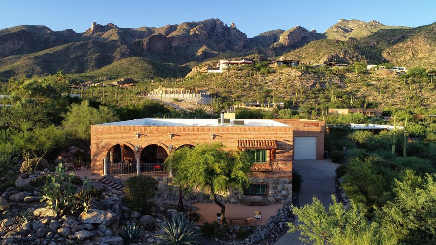 A stunning one-of-a-kind retreat perched high in the Catalina Foothills in the shadow of famed Finger Rock, with Old Tucson charm yet masterfully and tastefully updated, with the potential to be multi-generational or to accommodate a private practice with a separate entrance, is now available for your perusal. It's on a cul-de-sac with very little traffic, fabulous privacy and an opportunity for quiet enjoyment of nature. A welcoming front terrace is a delightful spot to relax and enjoy the views and lights of downtown Tucson. Enter into an open foyer with a glassed-in stairway to lower level, a bright and airy space that could accommodate a tall sculpture or mobile. With a unique floor plan, the two levels of this charming home provide multiple spots to live and gather. The entry level provides a full living area with kitchen, powder room, dining room, breakfast nook, living room, large master suite, guest room with en-suite bath, and a wonderful rear terrace with fireplace and reach-out- and-touch views of Finger Rock and the Catalinas. The lower level is fabulous, with another large master suite, two additional bedrooms, a den and office/study/ library area, a stunning wet bar and a 600-bottle wine cellar. On the entry level, be sure to look up to view the 9' tall handsomely beamed wormwood ceilings. And note the genuine hardwood flooring as well. 
The kitchen is stylishly updated with handsome Brazilian stone counters and stainless Kitchen Aid appliances including 2 convection ovens and a six burner gas stove. There is a prep sink in the island, pull-out features in lower cabinets, built-in tray and lid storage, and a terrific walk-in pantry. Leaded glass cabinet doors add extra charm. Enjoy breakfast or supper looking out to the gorgeously landscaped rear yard and up to Finger Rock and the other peaks of the Catalinas. Even an adjacent powder room has "OMG" views! The dining room is a warm and comfortable space with views of lush desert plantings, city lights and the distant mountains to the south, with a sliding glass door out to the entry terrace. The graciously large living room is focused on the handsome Canterra stone wood-burning fireplace which is one of many warm gathering spots. Double glass doors lead to the rear terrace with another welcoming fireplace, overlooking the gorgeously landscaped rear yard and with wrap-around stunning views of the Catalinas and the mountains of East Tucson. The upstairs master suite likewise opens to this terrace and also enjoys views toward the mountains of East Tucson. With a brick wall, richly shaded built-in bookshelves and entertainment center and a sitting area, it's a welcoming space. An en-suite second bedroom also enjoys a custom sink set in an antique-style bureau. 
Head down the polished wooden stairs to enjoy the lower level for the large open family room with polished brick floors and adjacent study/office space. French doors lead out to a lower level screened-in patio, or "Arizona Room" with cozy with another charming fireplace surrounded by custom tilework and direct access to the gardens and multiple sitting areas in the yard. A lap pool (with a motorized pool cover) with 4 "endless" jets for exercise is also in the yard.  Back inside, the generously sized wet bar with gorgeous glass tile top beckons. Beyond is the 600 bottle wine cellar, behind hermetically sealed glass doors, that won a design award from Sunset Magazine. It's lovely, elegantly lit and has room for a couple of bistro tables for wine tastings. What a spot to entertain! Nearby, a substantially sized 2nd master bedroom has handsome custom wood-framed glass doors out to the Arizona Room. The master bath for this suite is handsomely remodeled with travertine floors and travertine lining the glassed-in contemporary shower.  Sinks are set in attractive antique-style bureaus with marble tops. The oval soaking tub enjoys views across the Valley to the East Tucson mountains. A fourth bedroom features Saltillo tiles and accesses a full bath with glassed-in updated shower and another sink set in an antique style bureau, each one unique. A fifth  bedroom is presently outfitted as a "Closet For A Princess" with shelving, hanging space, a make-up table and its' own large walk-in closet; this space could be easily converted back into another bedroom. A large laundry room features an oversized stainless-steel utility sink. The rear yard features multiple sitting areas, one with a motorized shade and another inside a gazebo, and is a quiet private respite with only the sounds of the birds. There is an RV-capable garage (up to 31' RV) with an air-conditioned workshop, sink and loft, with an observation deck on top of the garage....wrap-around views of the entire Tucson Valley! Note the on-site parking for 3-4 vehicles, with stunning entry gardens leading up to the home. A couple of technical details: the exterior walls of the lower level are thick concrete block covered with fire brick so the downstairs stays cool...low electrical costs! Upper level and garage is adobe brick. There is a water pressure regulator and recirculating pump for the downstairs master shower. The upper deck is coated with an elastomeric coating that was professionally applied and will not be broken down by UV rays.  Dual zone Trane heat pumps with dual zone thermostats were recently installed.   Motorized pool cover keeps out debris and reduces costs for chemicals.  Of course, the location is "prime" with District 16 schools, easy access to the many amenities of the Foothills, and also to Tucson's excellent medical care. You are invited to come take a look, and to consider building your family's memories here as the current owners so enjoyed doing.