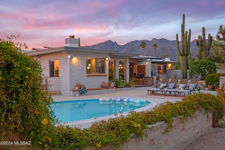 Sited on over an acre, this Midcentury Adobe home was designed by architect Dave Fraker. Abundant windows and a sprawling open plan position this home for premium views of our Tucson mountains and city lights. Floor to ceiling glass and modern design details make this home one of the finest in the Catalina Foothills. Quartz countertops, stainless steel appliances, and custom pantry complete the well appointed kitchen. The primary suite offers two walk-in closets, kiva fireplace (one of four fireplaces in the home), and spacious updated bathroom. Two additional bedrooms and a den/office overlooking the pool and skyline. The grounds include a pool, sport court, saguaro studded veranda, and ample parking. Just a short drive to hospitals, schools, and The Loop (rillito bike path). Owned solar, blown-in insulation, energy efficient tankless water heater, commercial grade exterior doors, roll down shutter and a whole house generator. This home offers superb energy efficiency.