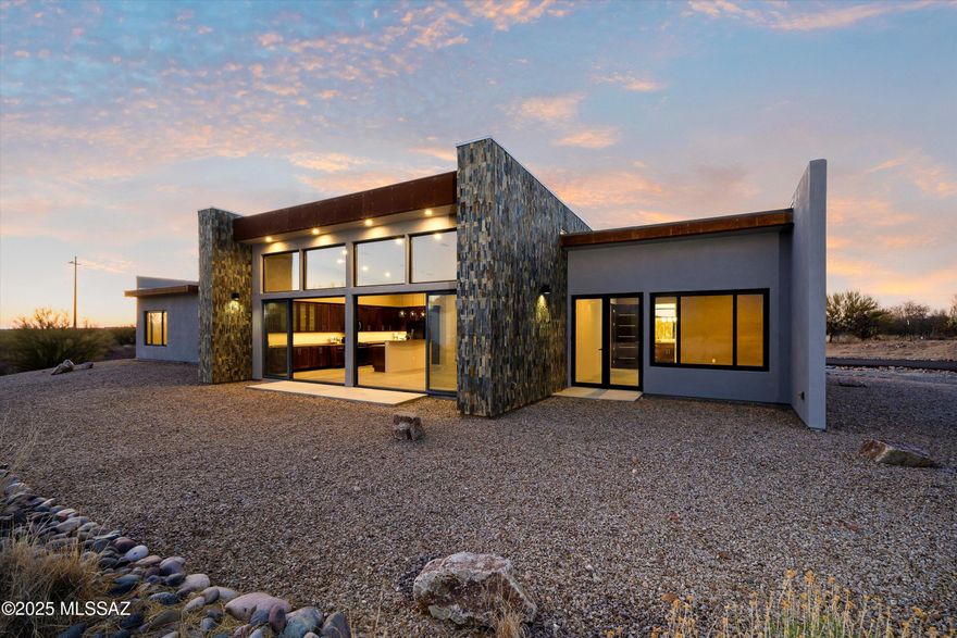 Welcome to North Dust Devil Drive, where the mountains aren't just a view—they're your backyard. Designed by SBBL Architecture with site layout by architect Rob Bass to maximize views and energy efficiency, this 4-bedroom, 3.5-bath contemporary retreat spans over 3,000 square feet on a full private acre with no HOA.
Dramatic custom metal entry doors open to reveal where contemporary architecture meets the raw beauty of the Sonoran Desert. The striking exterior showcases a masterful blend of stacked stone, sleek stucco, and metal accents—the stone-covered parapeted foundation walls creating the same visual angles as the mountains themselves, casting shadows that mimic the Catalinas at sunset.
Step inside where concrete floors flow seamlessly through every room—low-maintenance, durable, and perfectly suited to desert living. The great room captivates with dramatic vaulted ceilings soaring to 13 feet and walls of commercial-grade windows featuring double pane, argon-filled tempered glass with superior UV protection. The home's strategic orientation maximizes winter sun while minimizing summer heat gain smart passive solar design. The sliding glass doors erase the boundary between inside and out, creating a seamless flow perfect for entertaining against Arizona's legendary sunset backdrop. Recently installed weatherproof shutters mean you can button up for monsoon season or when you travel, then open back up to those views that never get old. 
The chef's kitchen is where functionality meets sophisticated design. Premium birch wood shaker-style cabinetry with sleek hardware provides storage and striking contrast against gleaming high-end stone countertops strategically positioned to maximize mountain views. Contemporary slate stainless appliances blend seamlessly while a generous island becomes the natural gathering spot. Custom built-in buffet cabinets along the dining area wall define the space beautifully. The eat-in area offers mountain views, and even that sink overlooks the Catalinas.
Your primary suite is tucked into a split-bedroom floor plan for complete privacy. Imagine starting each day with mountain views, then stepping through sliding glass doors to your secluded patio. The spa-worthy bathroom features a dramatic floor-to-ceiling stacked stone feature wall in carefully selected light neutral tones, sculptural freestanding tub, and oversized glass shower. The custom walk-in closet system with rich wood finishes is beautifully organized.
Three additional bedrooms give you options for guests, office, gym, or whatever your life requires. One features its own ensuite bath with mountain views and walk-in showerperfect for visitors or multi-generational living. Two more bedrooms share the third full bathroom. Throughout the home, superior construction includes 2"x6" framing for exceptional structural integrity and noise reduction, high-density roof insulation, and heavy 8-foot custom wood composite doors.
An architectural standout: the impressive 6-foot wide main hallway with a window at the end that bathes the entire corridor in orange light at sunset transforming what could have been ordinary into something dramatic.
Here's what makes this property truly rare: that full acre on the outskirts of Oro Valley, with these views, and no HOA. The spacious three-car garage handles your vehicles while RV parking means your adventure mobile is always ready. Build the pool you've dreamed about. Add a guest casita. Create an outdoor kitchen and entertaining areas. Or preserve the pristine desert landscape and watch quail families parade through while javelinas root around at dusk.
You're minutes from Oro Valley's best shops and restaurants, yet you feel a world away. Catalina State Park and Coronado National Forest beckon with endless hiking, mountain biking, and exploration. Natural gas service and paved road access provide modern conveniences in this serene setting.
This isn't just a houseit's a lifestyle. Contemporary luxury meets desert tranquility, where every window frames a postcard-worthy view, and where your vision for desert living can unfold without limitation.
Come experience what it means to have the Catalinas as your backdrop for everyday living. Schedule your private tour today!