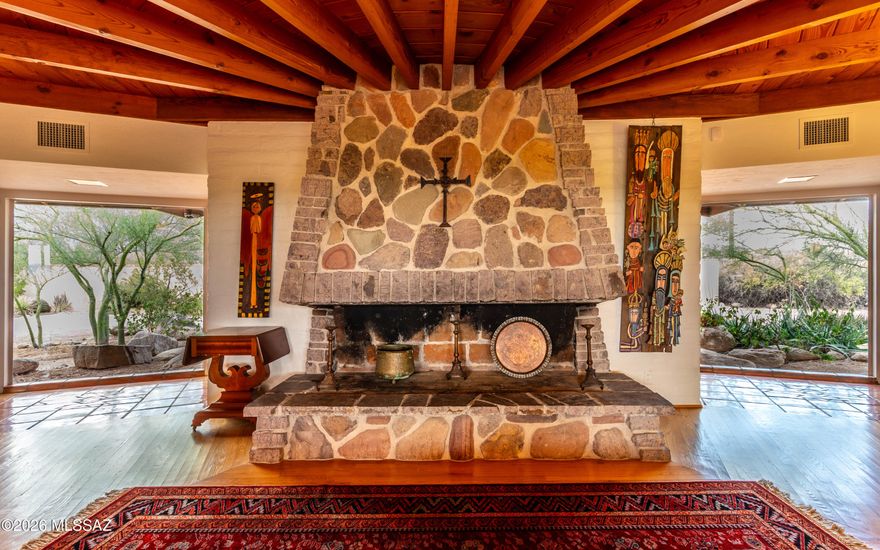 This one-of-a-kind midcentury burnt adobe was once owned by famed industrialist Howard Hughes. Distinctive character is evident throughout, beginning with the living room's rhyolite stone fireplace framed by wood beam ceilings that create an architectural focal point. The spacious family room features Mexican tile floors and a second fireplace. There's an office off the family room providing extra versatility. The kitchen retains its original custom mahogany cabinetry, now paired with quartz and butcher block countertops. The primary suite includes a dressing area with built-in cabinetry and dual closets. All three bedrooms open to the wide covered patio through sliding glass doors, inviting indoor-outdoor living. Enjoy city lights and sunset views from the back patio. Don't miss the extended-length 2-car garage with workshop space next to a third covered parking space.