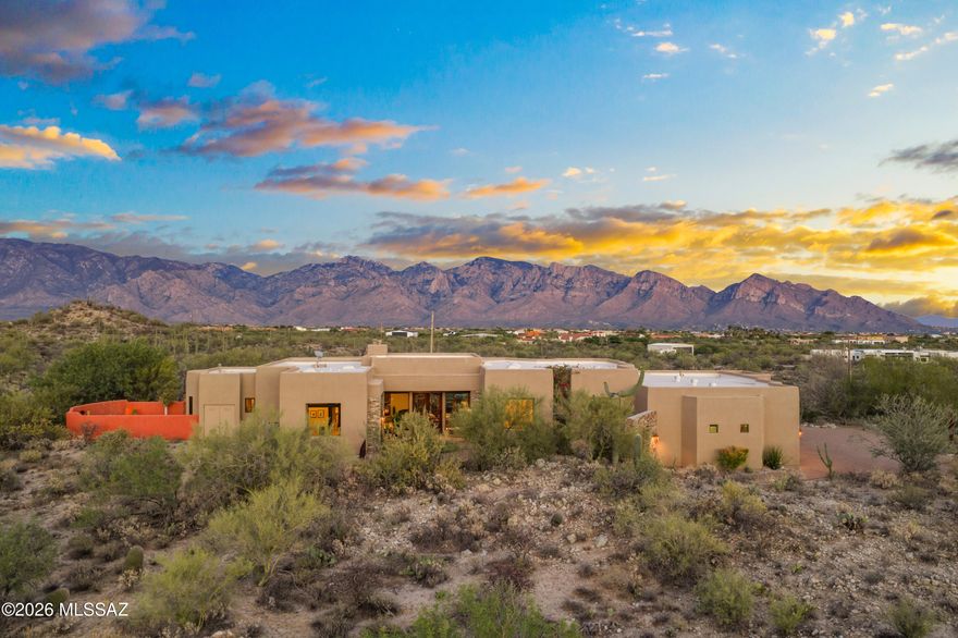 Set against the breathtaking backdrop of Southern Arizona's high desert, this home offers a rare opportunity to own a private luxury estate on nearly 5 acres with sweeping Catalina and Tortolita Mountain views and sparkling city lights beyond. Priced at $1,289,000, this exceptional property blends timeless Santa Fe architecture, modern comfort and unmatched serenity just minutes from Oro Valley amenities, shopping, dining and recreation. Built in 2009 and thoughtfully designed for both everyday living and entertaining, this 3,741sf 3BR/3 ½BA home is anchored by a spacious great room concept featuring a cozy fireplace, flush-mount speakers and abundant natural light. Travertine and wood flooring, along with coffered and tray ceilings, are carried throughout the home, creating a cohesive and elevated design. A stunning 16-foot glass door opens to expansive patios, creating seamless indoor-outdoor living against a dramatic desert backdrop. The home is constructed on a post-tension slab for enhanced structural integrity and efficiency. The chef's kitchen is a true centerpiece with granite countertops, custom wood cabinetry, large center island, walk-in pantry and premium Wolf and Sub-Zero stainless appliances. A generous dining nook and den provide flexibility for both casual and formal gatherings. The luxurious primary suite is a private retreat offering direct patio and pool/spa access, its own gas fireplace and a spa-inspired bath with dual vanities, soaking tub, oversized walk-in shower with multiple shower heads and two large walk-in closets. Separate-entry bonus room offers exceptional flexibility for today's lifestyle. Ideal as a private home office, artist studio, fitness space, media room or hobby area, this light-filled room is set apart from the main house, providing a quiet, dedicated environment for work or creativity. A rare feature that enhances both function and privacy without disrupting the main living space. Step outside and experience resort-style living at its finest. The property captures panoramic 360-degree views, enhanced by a large covered patio with ceiling fans, pool/spa, built-in BBQ and entertaining area, tranquil koi pond with waterfall and beautifully maintained mature desert vegetation. A greenhouse adds a unique opportunity for year-round gardening, while the fenced backyard provides additional privacy and usability. Paver stone accents extend through the circular driveway and outdoor living areas, complemented by elegant iron gates and trellis features that enhance the home's architectural charm. Additional highlights include an oversized 3-car garage with extensive storage, a dedicated office with private entrance ideal for working from home, two guest bedrooms with en-suite baths, custom solid wood doors and stone architectural details, central vacuum system, fire sprinkler system, 8 skylights, two HVAC systems, two newer water heaters (2025), a newer chip seal driveway and no HOA. This Tucson luxury home delivers the perfect balance of privacy, space and convenience, making it ideal for those seeking a desert retreat with upscale finishes and unforgettable views. Homes with this level of acreage, views and quality rarely come available.
