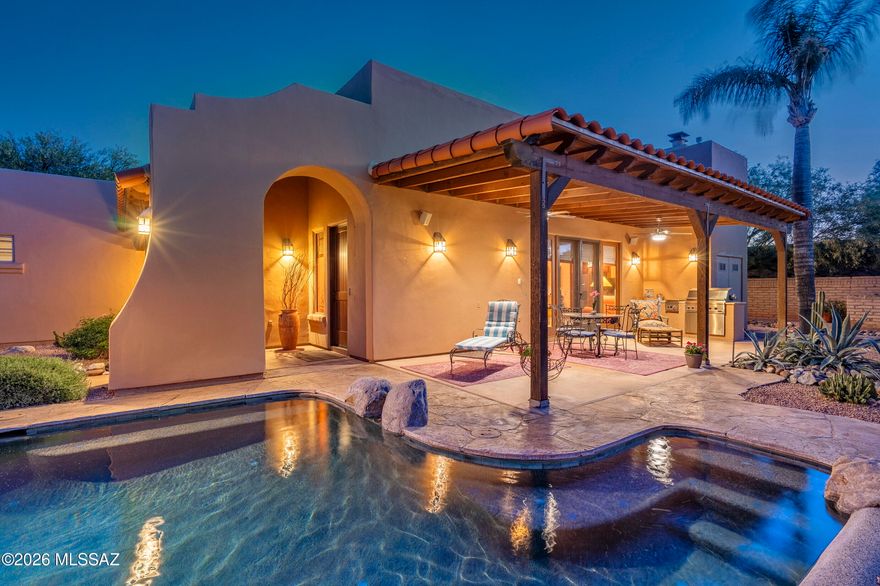 Situated within the gated enclave of The Garrison in the Old Fort Lowell Historic District, this residence offers a level of architectural presence and design integrity that is both rare and immediately felt. A graceful arched entry introduces a private, walled courtyard, setting a tone of understated sophistication and intentional privacy from the moment of arrival. Inside, the home unfolds with a striking sense of volume and light. Soaring ceilings, articulated by exposed wood vigas, create a dramatic vertical scale, while clerestory windows are positioned with precision, allowing natural light to enter as a dynamic element within the space. Throughout the day, light shifts and softens, subtly transforming the interiors and shaping the overall atmosphere. The result is an environment that feels expansive yet grounded, where openness and light influence the experience of the home in a way that is both calming and quietly compelling. Stained concrete floors anchor the space, complemented by softly contoured walls and a refined, cohesive material palette.

The Great Room serves as the architectural and social center of the home, where living, dining, and kitchen spaces flow together seamlessly. Expansive glass doors and large format windows frame views into the surrounding courtyard, dissolving the boundary between indoors and out while amplifying both scale and livability.
The kitchen is cleanly integrated yet distinctly appointed, featuring rich cherry wood cabinetry carried throughout the residence, paired with slab granite countertops and a full height granite backsplash. A professional grade stainless steel range and hood create a strong focal point, while the center island with bar seating extends naturally into the living space, offering both function and connection.

The primary suite is privately positioned and generously scaled, with direct access to the courtyard and a soft infusion of natural light. The ensuite bath reflects a continuation of the home's material language, with dual vanities, a soaking tub set within a tiled surround, and a glass enclosed shower with detailed tile work, all executed with restraint and consistency. Secondary spaces offer flexibility and thoughtful separation, each maintaining a connection to light and outdoor access.

At the center of the home, an all encompassing courtyard wraps around three sides of the residence, serving as both the visual anchor and the defining lifestyle element. A pool with a natural rock water feature introduces movement and texture, while covered patios, exposed beams, and multiple seating areas create a series of outdoor rooms designed for both gathering and retreat. Masonry walls and curated desert landscaping provide a sense of enclosure and privacy, while multiple points of access from within the home reinforce a seamless indoor outdoor experience.
